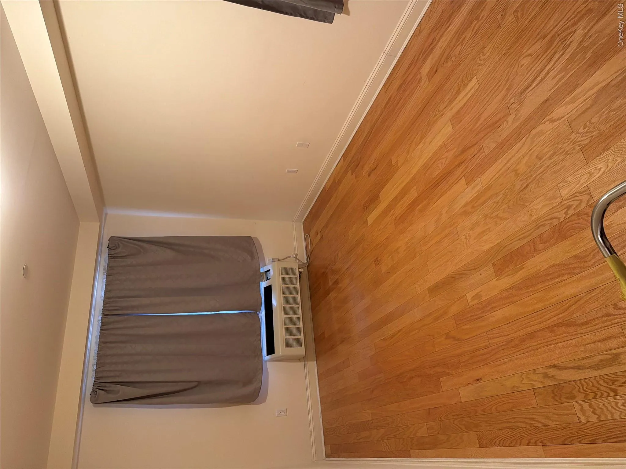 Hardwood flooring throughout, featuring baseboard molding, a window with curtains, and a wall-mounted air conditioning unit Hardwood flooring throughout, featuring baseboard molding, a window with curtains, and a wall-mounted air conditioning unit