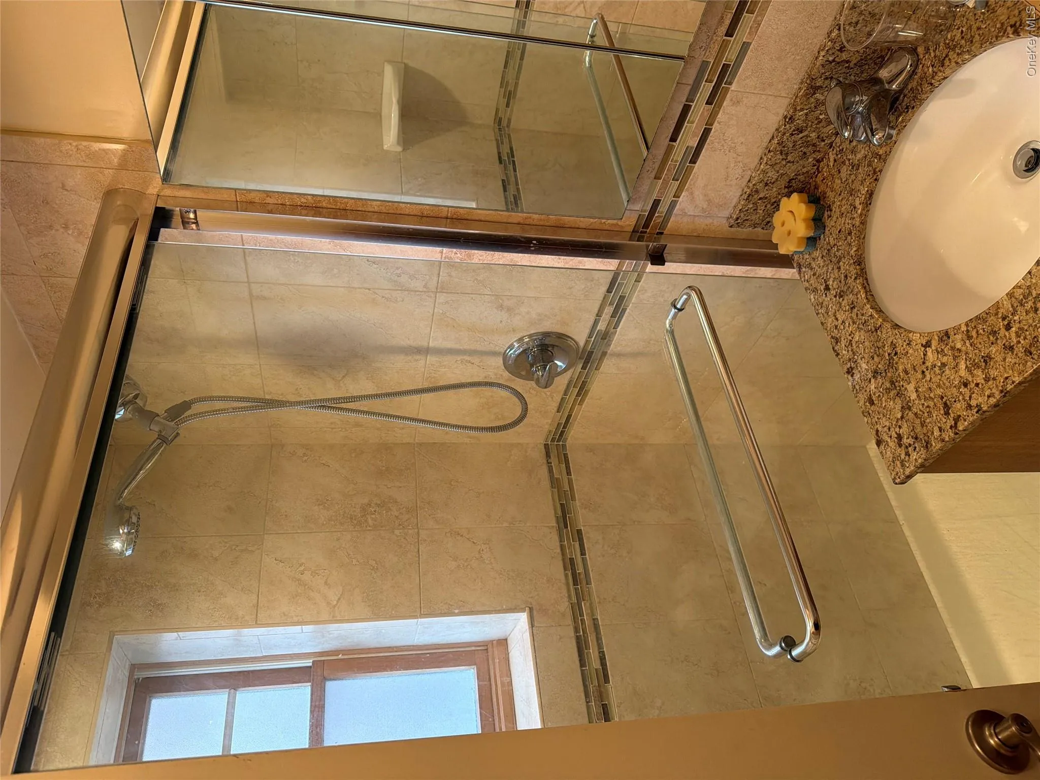 Bathroom featuring a glass-enclosed shower with a handheld shower head, tiled walls, and decorative accent border Bathroom featuring a glass-enclosed shower with a handheld shower head, tiled walls, and decorative accent border
