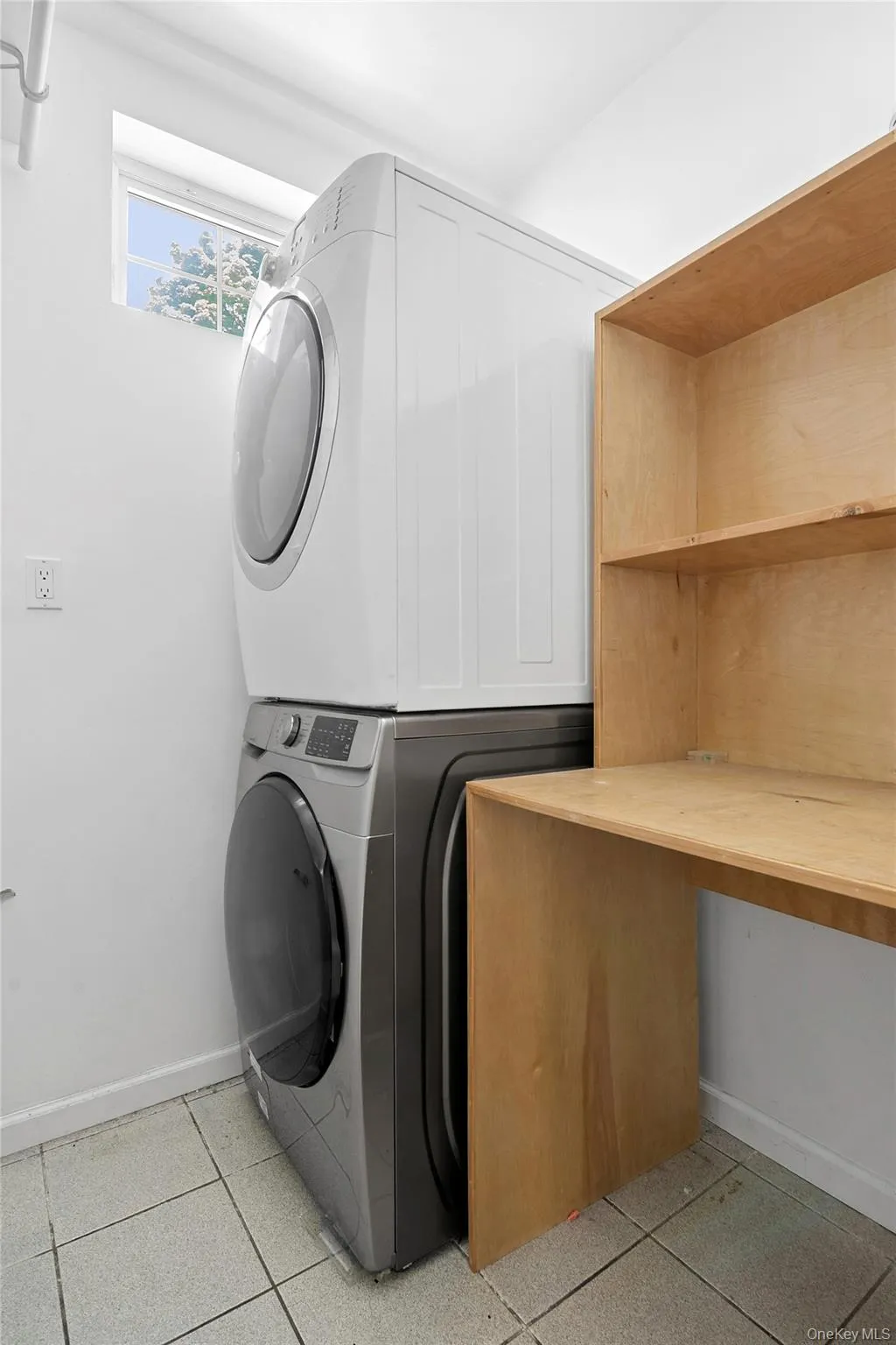 Dedicated laundry space featuring stacked appliances, built-in wooden shelving, a convenient workspace, and tiled flooring Dedicated laundry space featuring stacked appliances, built-in wooden shelving, a convenient workspace, and tiled flooring