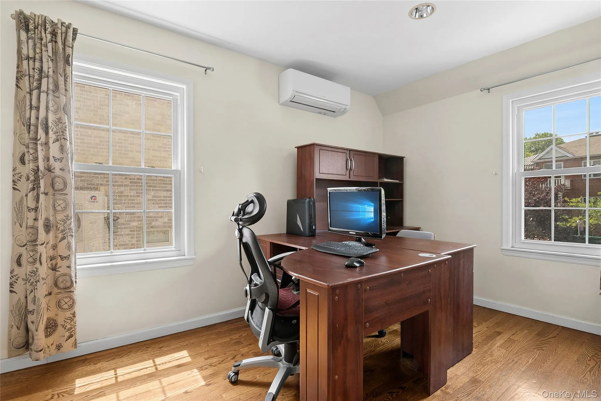 Third Bedroom/ Office featuring wood-finish flooring, two large windows with white trim, and a wall-mounted climate control unit Third Bedroom/ Office featuring wood-finish flooring, two large windows with white trim, and a wall-mounted climate control unit