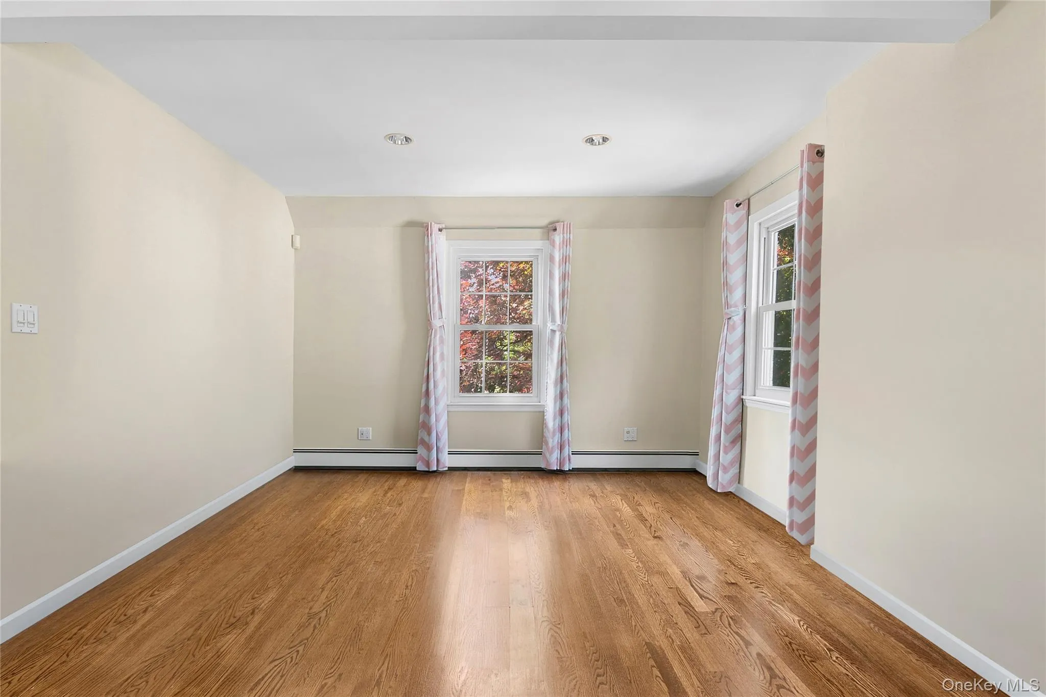 Primary Bedroom featuring wood-finish flooring, two double-hung windows, recessed lighting, and light-toned walls Primary Bedroom featuring wood-finish flooring, two double-hung windows, recessed lighting, and light-toned walls