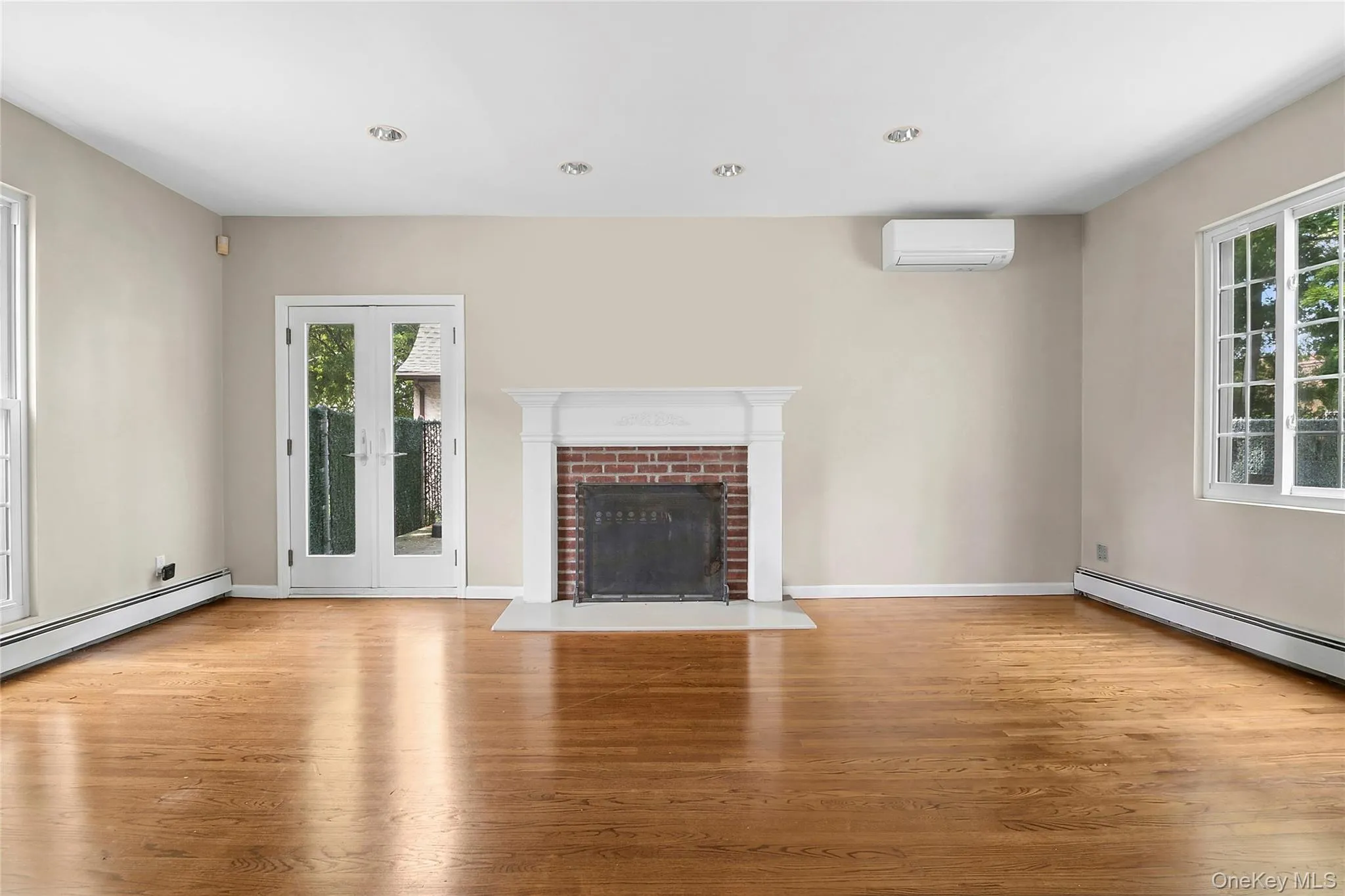 Spacious room featuring wood-finish flooring, a brick fireplace with a white mantel, and recessed ceiling lighting split AC Spacious room featuring wood-finish flooring, a brick fireplace with a white mantel, and recessed ceiling lighting split AC