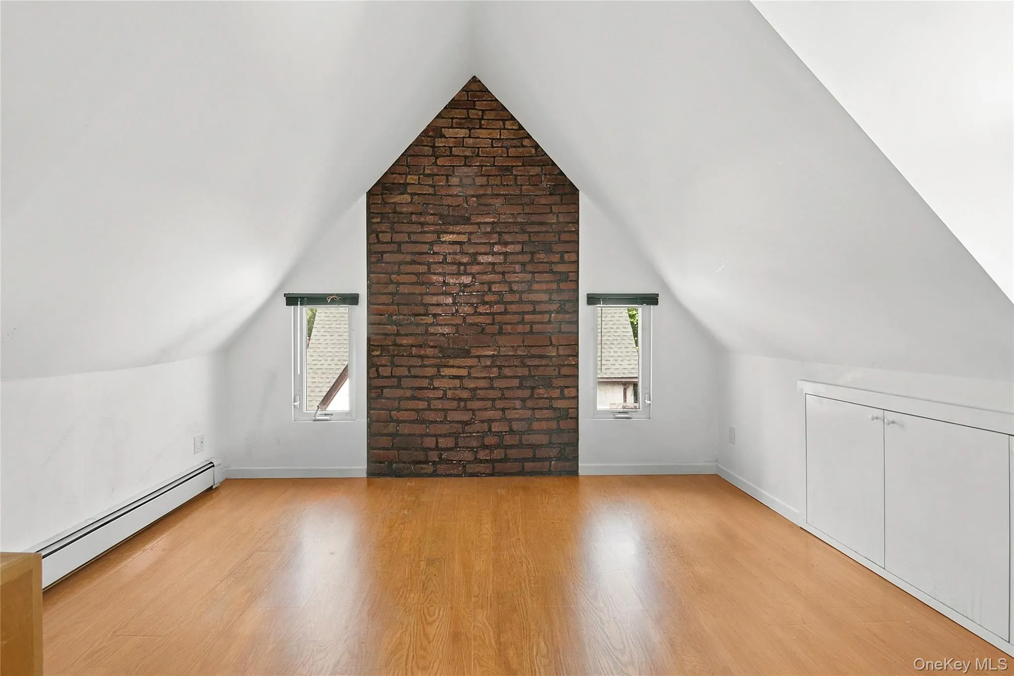 Bedroom 4 featuring a prominent exposed brick accent wall, two window openings, built-in lower cabinetry, and wood-finish flooring Bedroom 4 featuring a prominent exposed brick accent wall, two window openings, built-in lower cabinetry, and wood-finish flooring