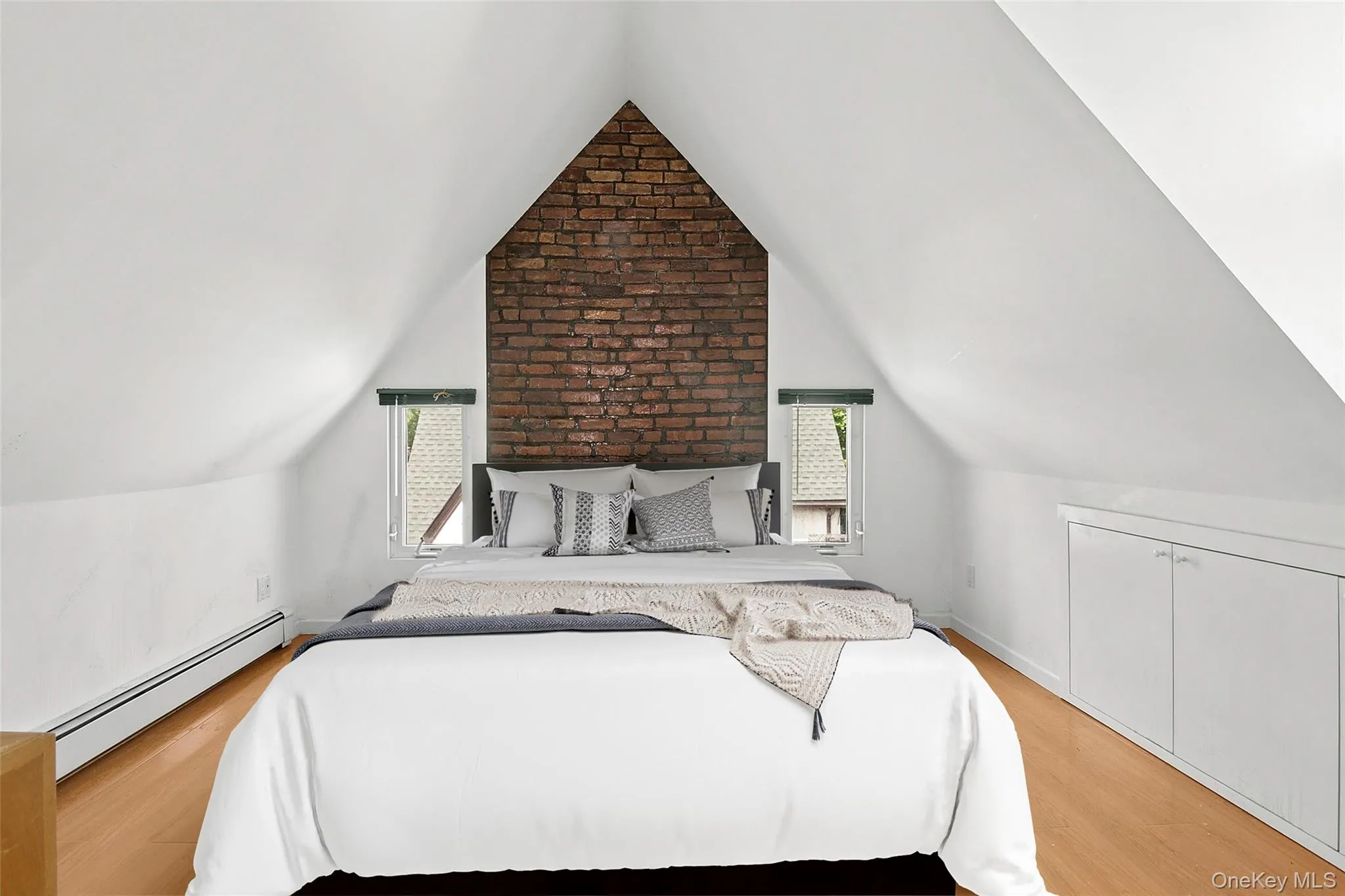 Virtually Staged Bedroom Four featuring an exposed brick accent wall, two window openings, built-in lower cabinetry, and wood-finish flooring Virtually Staged Bedroom Four featuring an exposed brick accent wall, two window openings, built-in lower cabinetry, and wood-finish flooring