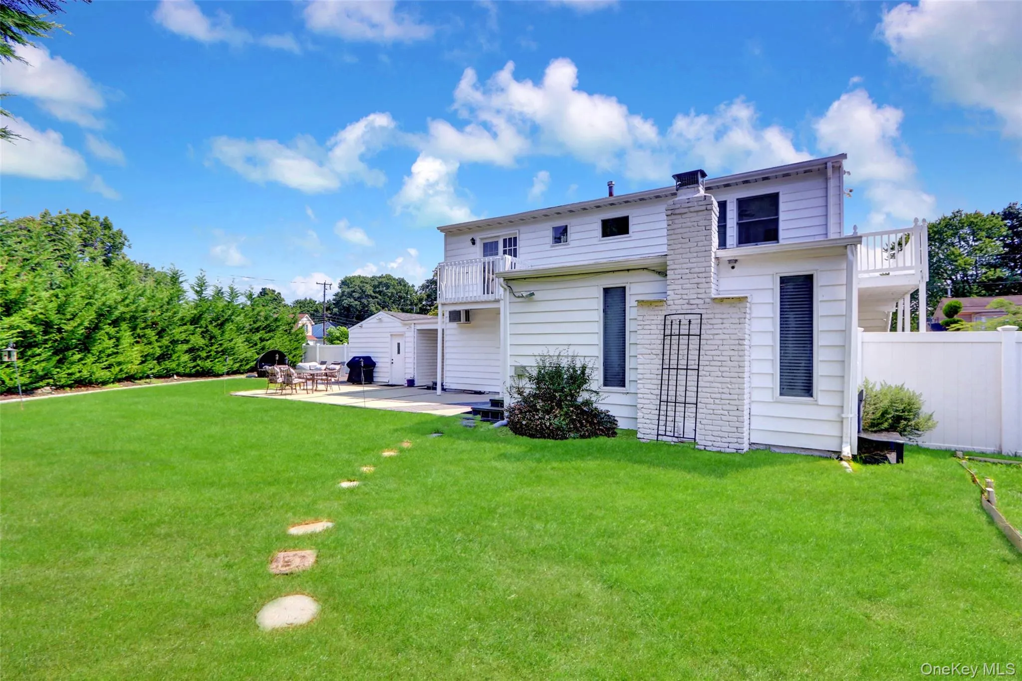 Expansive backyard featuring a large green lawn, concrete patio, white privacy fencing, and mature perimeter hedging Expansive backyard featuring a large green lawn, concrete patio, white privacy fencing, and mature perimeter hedging