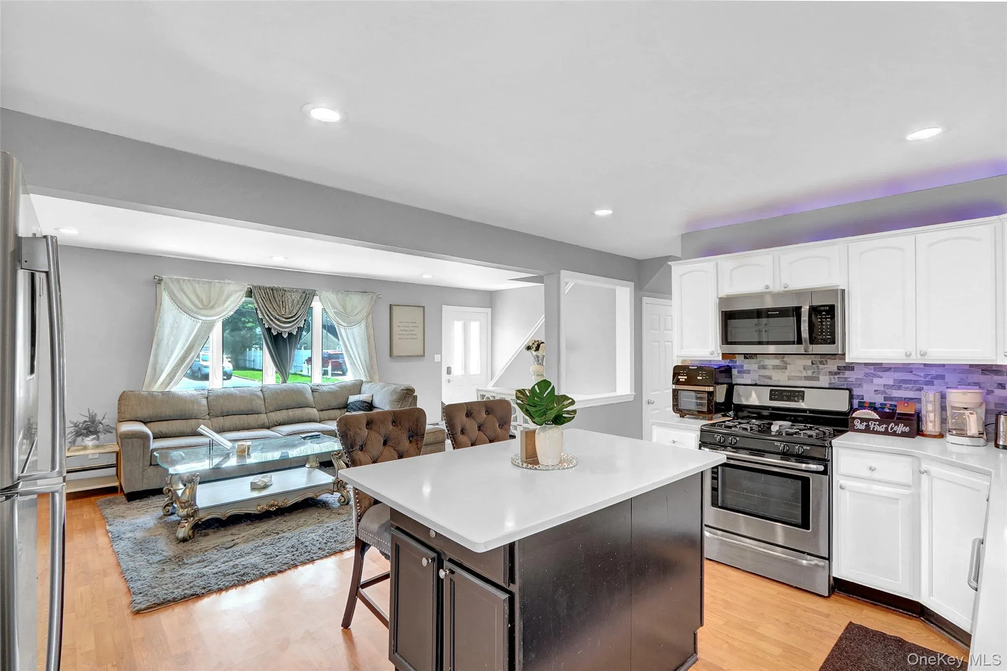 Open-concept living space featuring a central kitchen island with seating, stainless steel appliances, light wood-finish flooring, and recessed lighting throughout Open-concept living space featuring a central kitchen island with seating, stainless steel appliances, light wood-finish flooring, and recessed lighting throughout