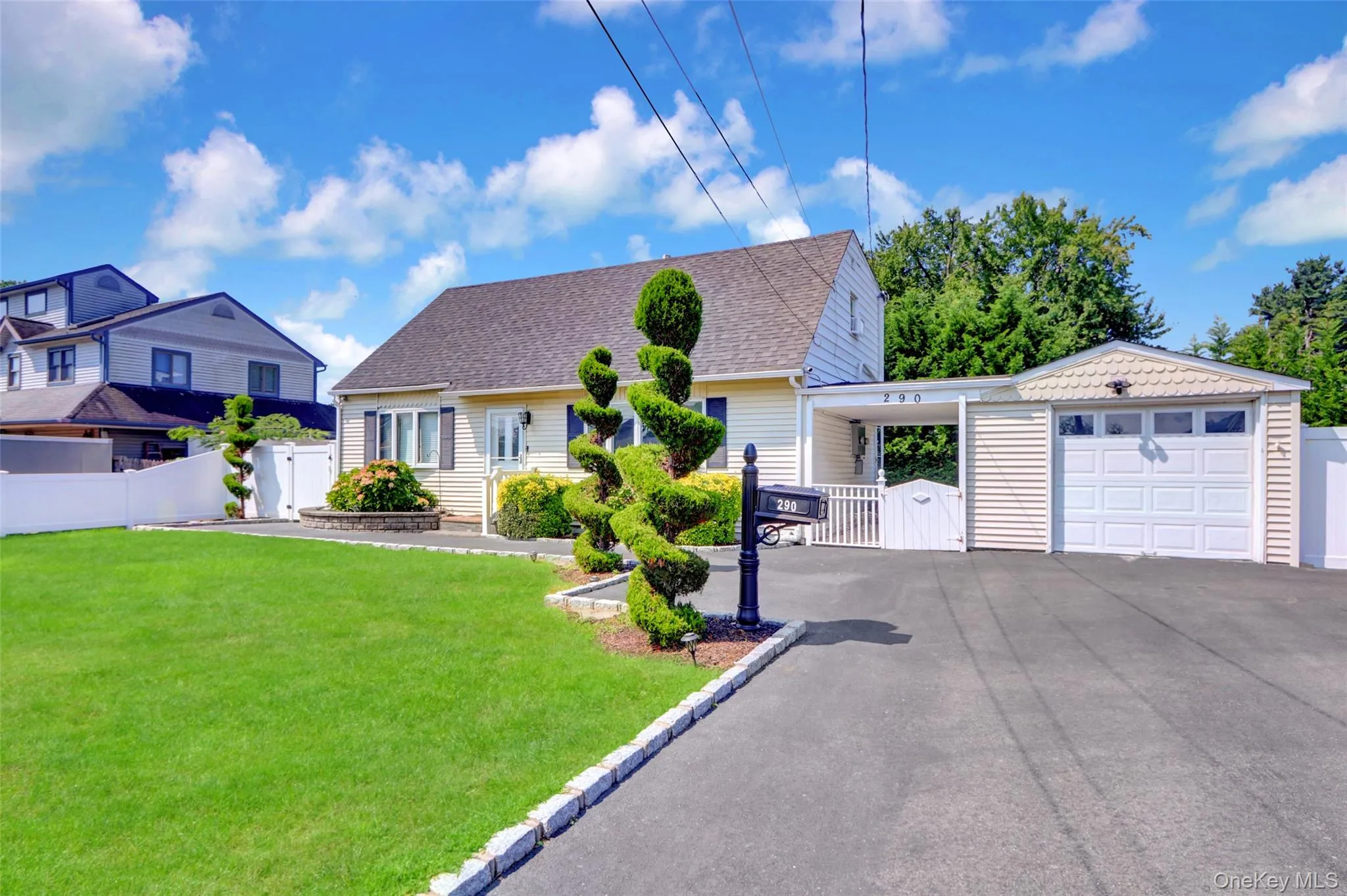 Exterior featuring a manicured lawn, paved driveway, attached garage, white picket fence, and mature landscaping Exterior featuring a manicured lawn, paved driveway, attached garage, white picket fence, and mature landscaping