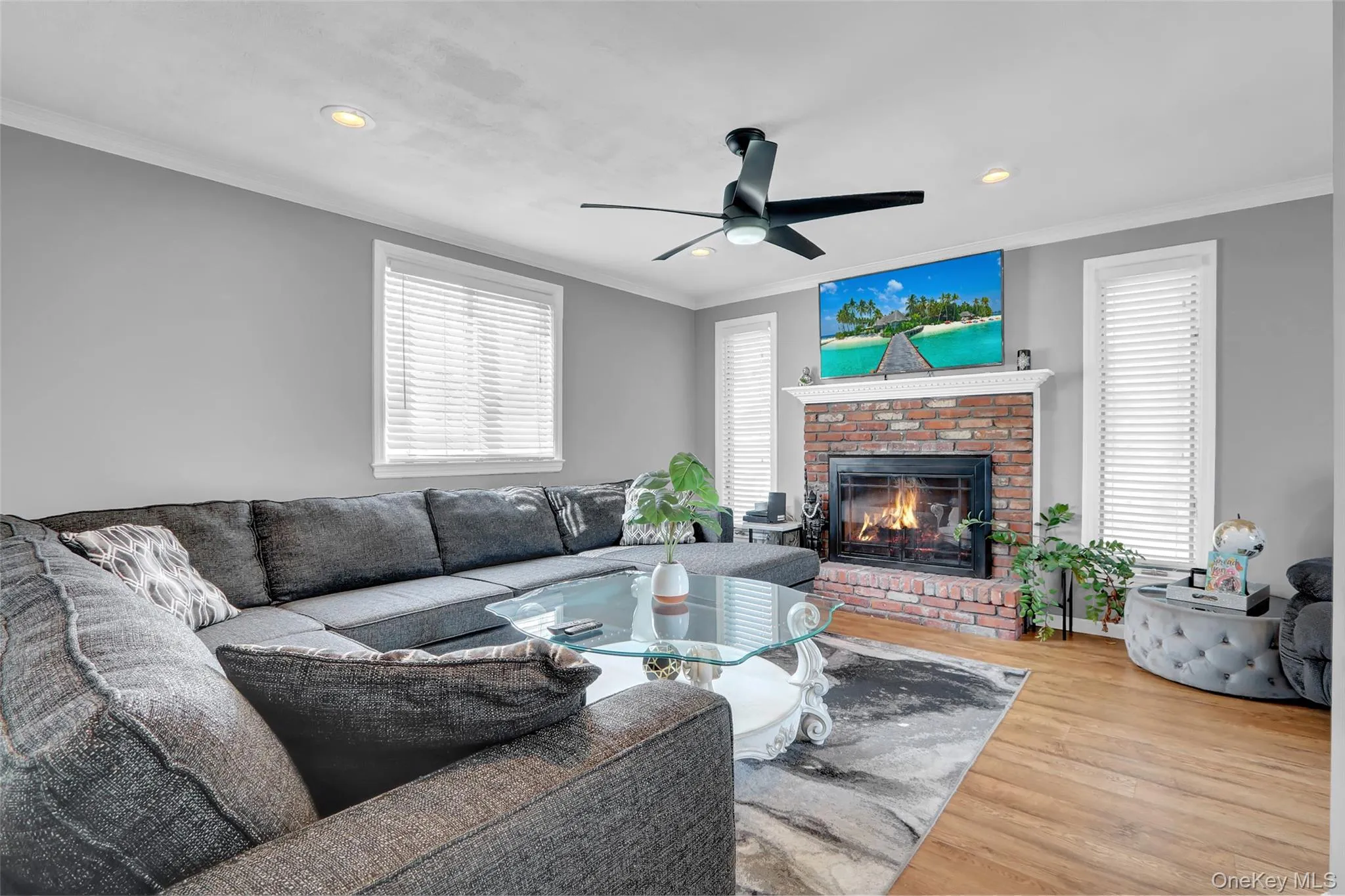 Living area featuring a brick fireplace with a white mantel, wood-finish flooring, recessed lighting, and a modern ceiling fan Living area featuring a brick fireplace with a white mantel, wood-finish flooring, recessed lighting, and a modern ceiling fan