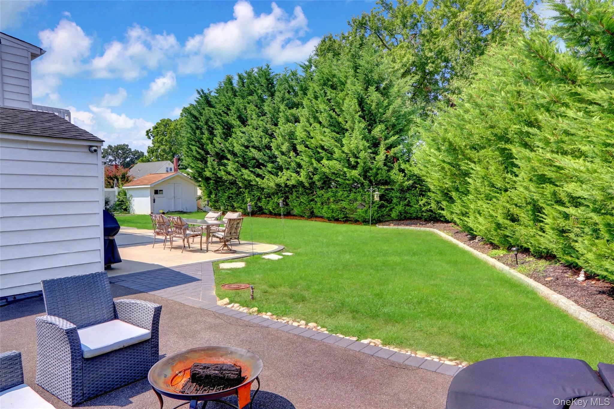 Expansive backyard featuring a lush lawn, established privacy hedges, and multiple paver patio areas Expansive backyard featuring a lush lawn, established privacy hedges, and multiple paver patio areas