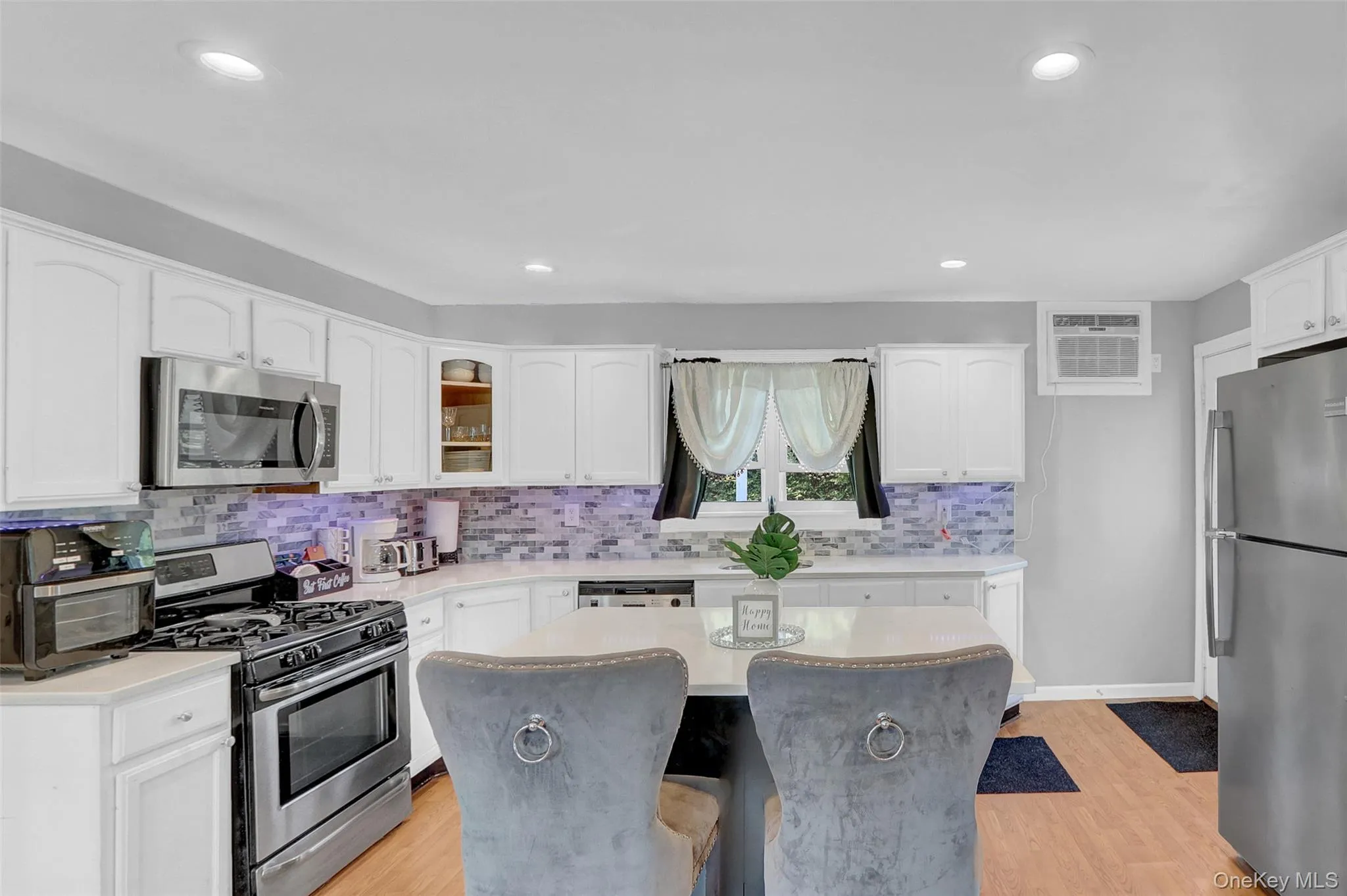 Kitchen featuring white cabinetry, stainless steel appliances, a mosaic tile backsplash, light-toned wood-finish flooring, and recessed lighting Kitchen featuring white cabinetry, stainless steel appliances, a mosaic tile backsplash, light-toned wood-finish flooring, and recessed lighting