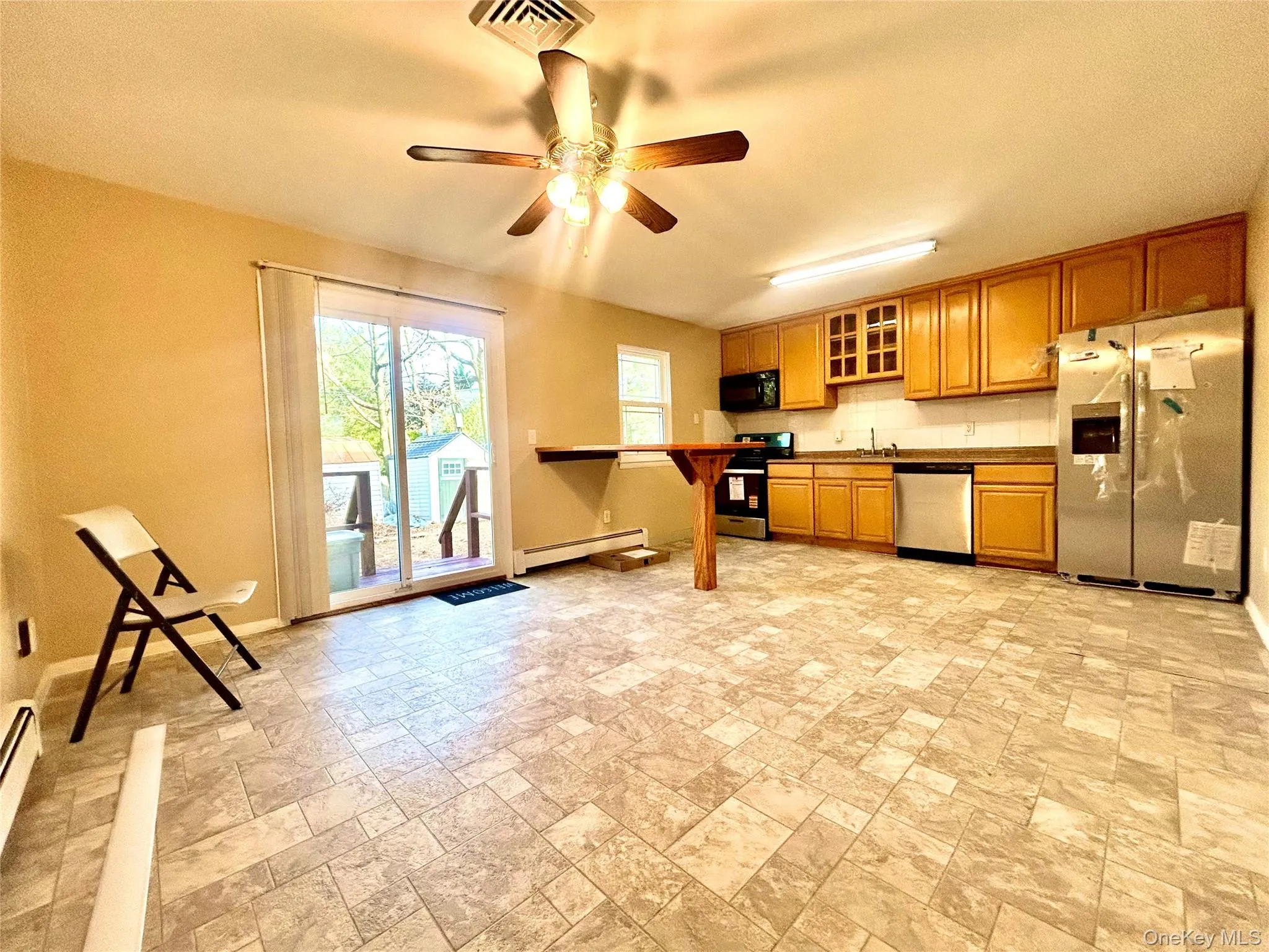 Kitchen featuring glass insert cabinets, appliances with stainless steel finishes, stone finish flooring, brown cabinets, and a baseboard heating unit Kitchen featuring glass insert cabinets, appliances with stainless steel finishes, stone finish flooring, brown cabinets, and a baseboard heating unit