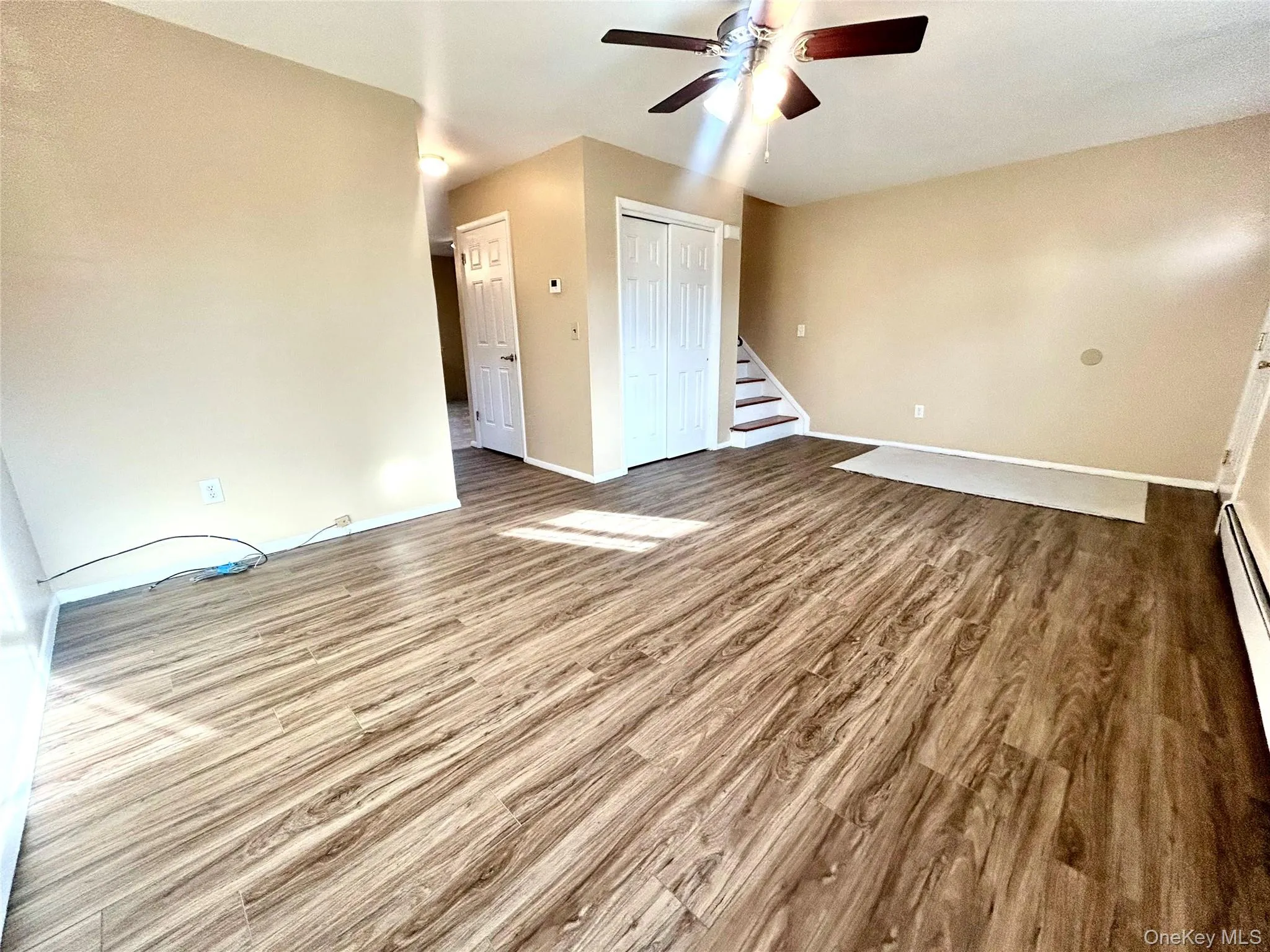 Unfurnished living room with ceiling fan, light wood-type flooring, stairs, and a baseboard radiator Unfurnished living room with ceiling fan, light wood-type flooring, stairs, and a baseboard radiator