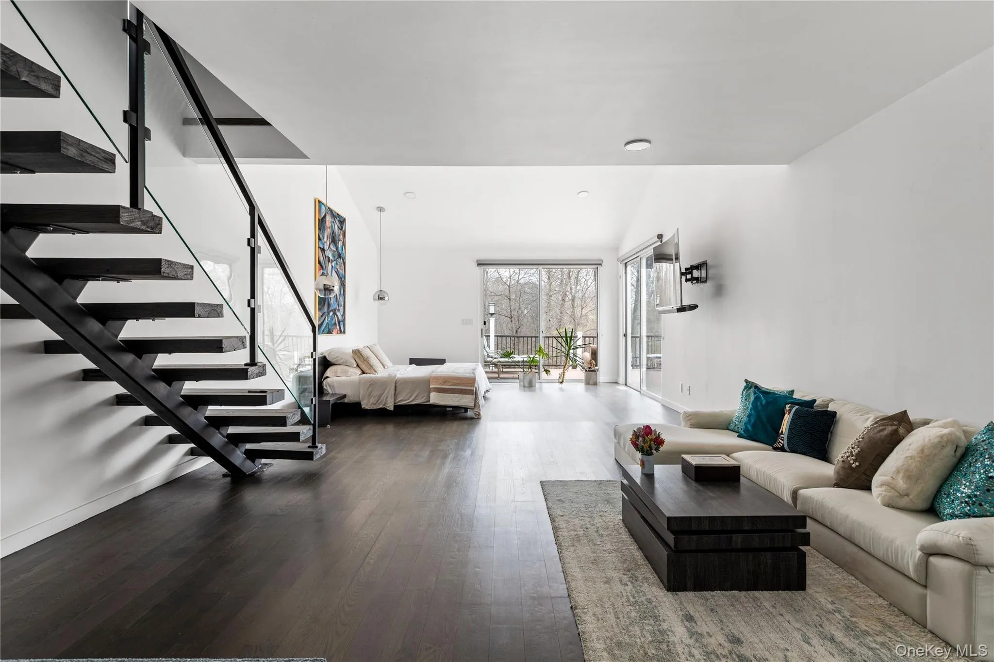 Sleek open-concept living space with dark wood-finish flooring, a modern floating staircase featuring glass railings, and a high vaulted ceiling Sleek open-concept living space with dark wood-finish flooring, a modern floating staircase featuring glass railings, and a high vaulted ceiling