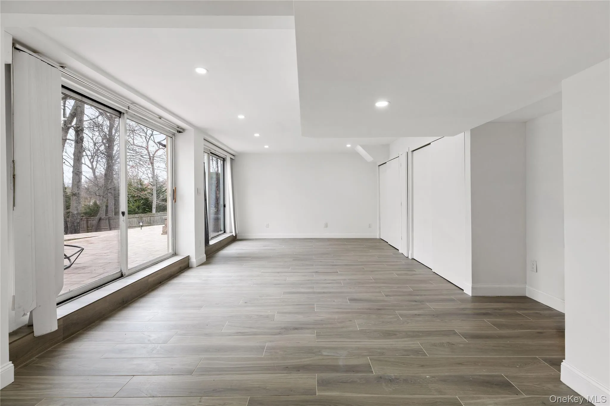 Spacious room featuring large sliding glass doors, recessed lighting, wood-finish flooring, and multiple built-in storage closets Spacious room featuring large sliding glass doors, recessed lighting, wood-finish flooring, and multiple built-in storage closets