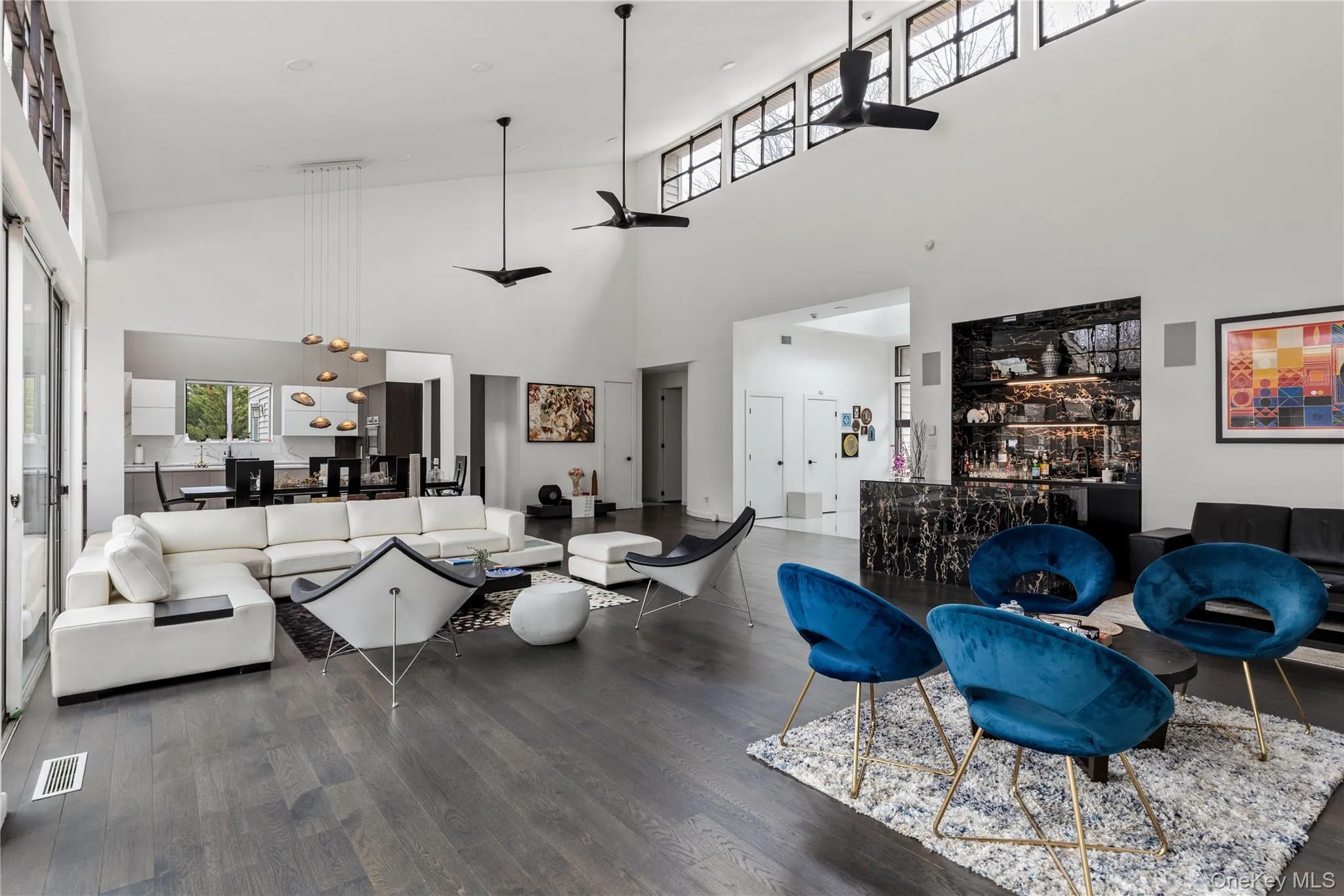 Vaulted living space featuring wood-finish flooring, high ceilings with clerestory windows, and a built-in wet bar with dark stone finishes Vaulted living space featuring wood-finish flooring, high ceilings with clerestory windows, and a built-in wet bar with dark stone finishes