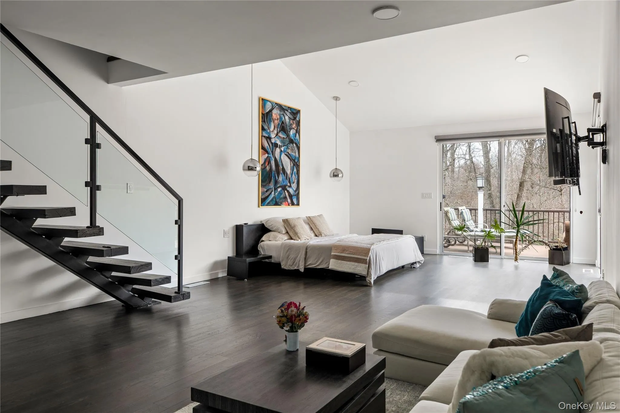 Open-concept interior featuring dark wood-finish flooring, a modern floating staircase with glass railing, and vaulted ceilings Open-concept interior featuring dark wood-finish flooring, a modern floating staircase with glass railing, and vaulted ceilings