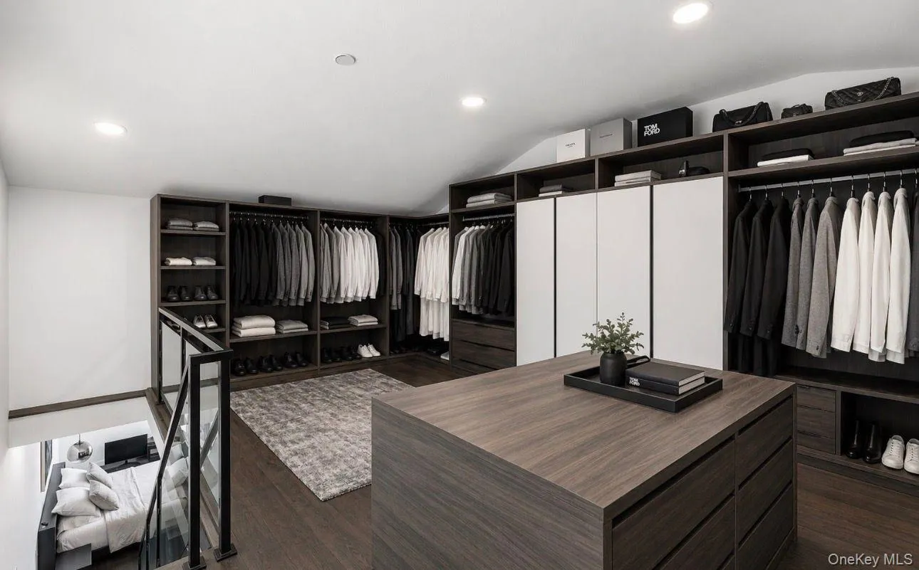 Expansive custom closet featuring recessed lighting, dark wood-finish cabinetry, integrated shelving and hanging storage, white panel doors, and a central island with drawer storage Expansive custom closet featuring recessed lighting, dark wood-finish cabinetry, integrated shelving and hanging storage, white panel doors, and a central island with drawer storage