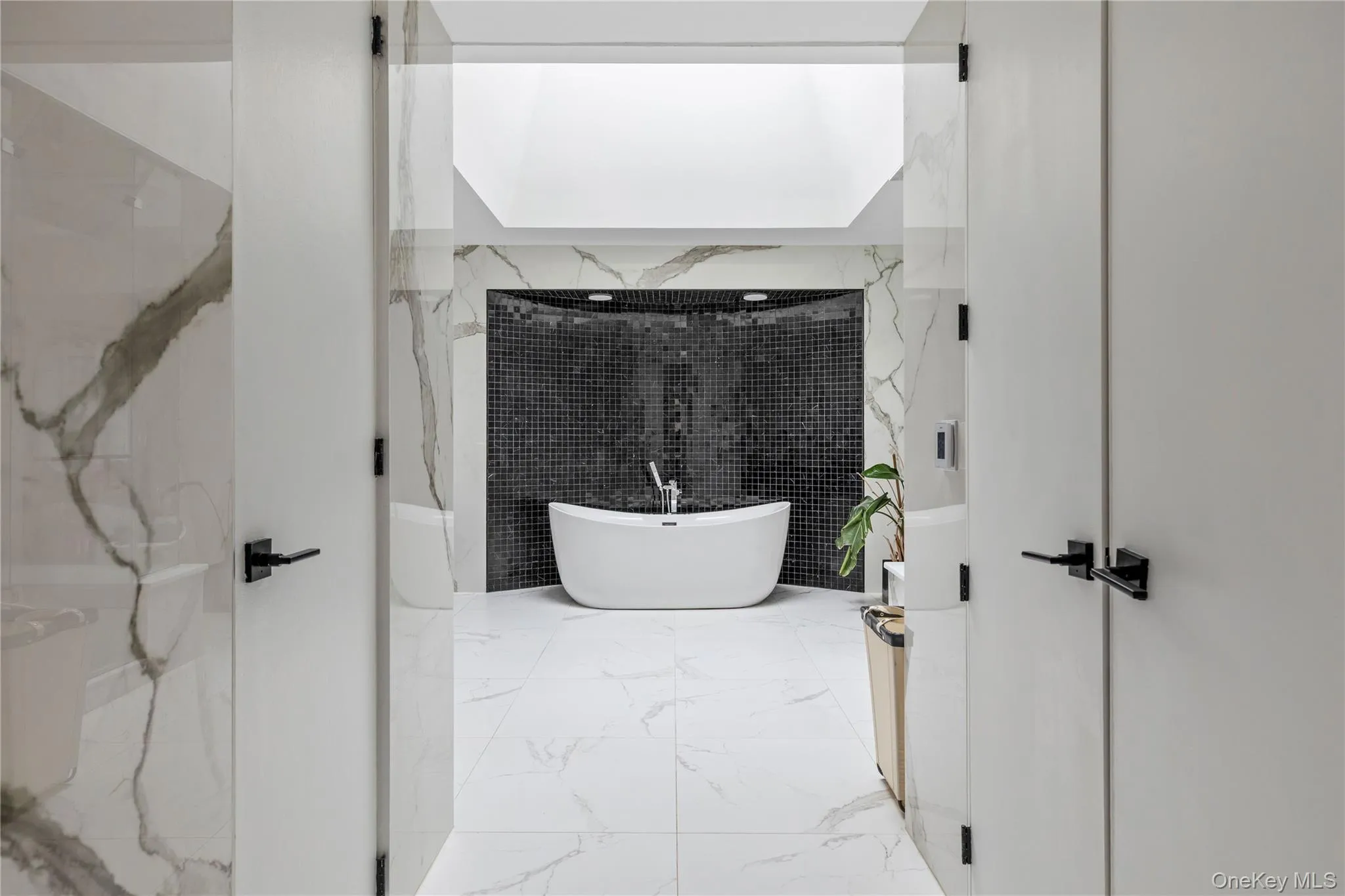 Sleek modern bathroom featuring an expansive freestanding soaking tub, black mosaic tile accent wall, and a large overhead skylight Sleek modern bathroom featuring an expansive freestanding soaking tub, black mosaic tile accent wall, and a large overhead skylight