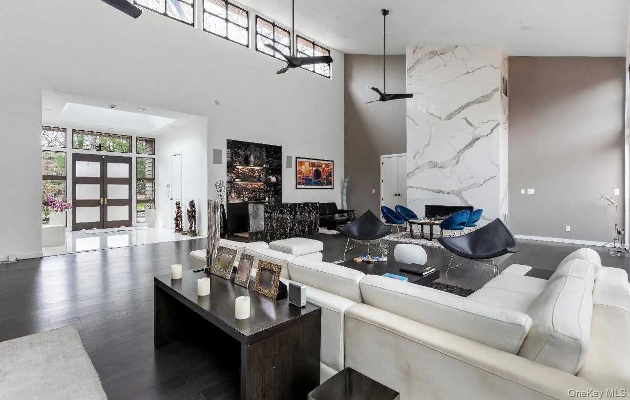 Spacious living area featuring a floor-to-ceiling accent wall with a linear fireplace, dark wood-finish flooring, and high ceilings with transom windows Spacious living area featuring a floor-to-ceiling accent wall with a linear fireplace, dark wood-finish flooring, and high ceilings with transom windows