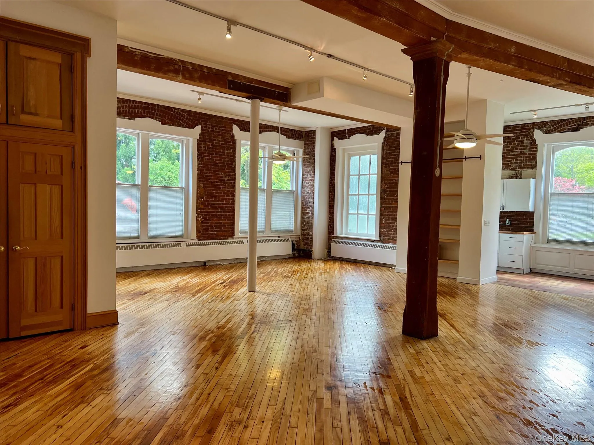 Empty room featuring ceiling fan, brick wall, light hardwood / wood-style flooring, and a baseboard heating unit Empty room featuring ceiling fan, brick wall, light hardwood / wood-style flooring, and a baseboard heating unit