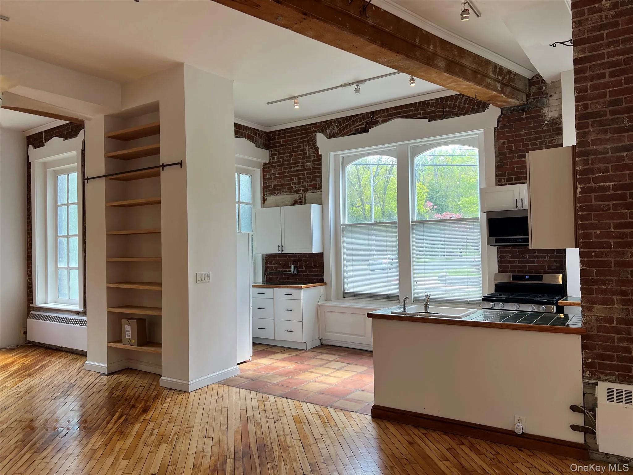 Kitchen featuring white cabinetry, light wood-type flooring, appliances with stainless steel finishes, tile counters, and radiator heating unit Kitchen featuring white cabinetry, light wood-type flooring, appliances with stainless steel finishes, tile counters, and radiator heating unit