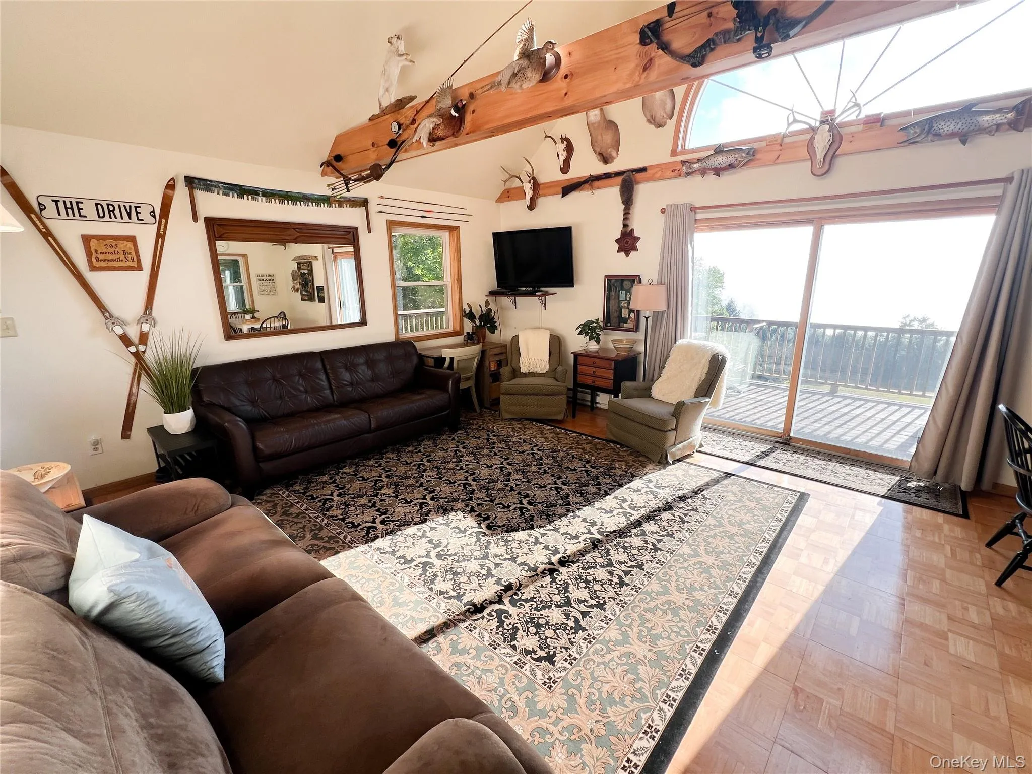 Living area featuring a vaulted ceiling with exposed wood beams, a large arched transom window, and expansive sliding glass doors opening to a deck Living area featuring a vaulted ceiling with exposed wood beams, a large arched transom window, and expansive sliding glass doors opening to a deck