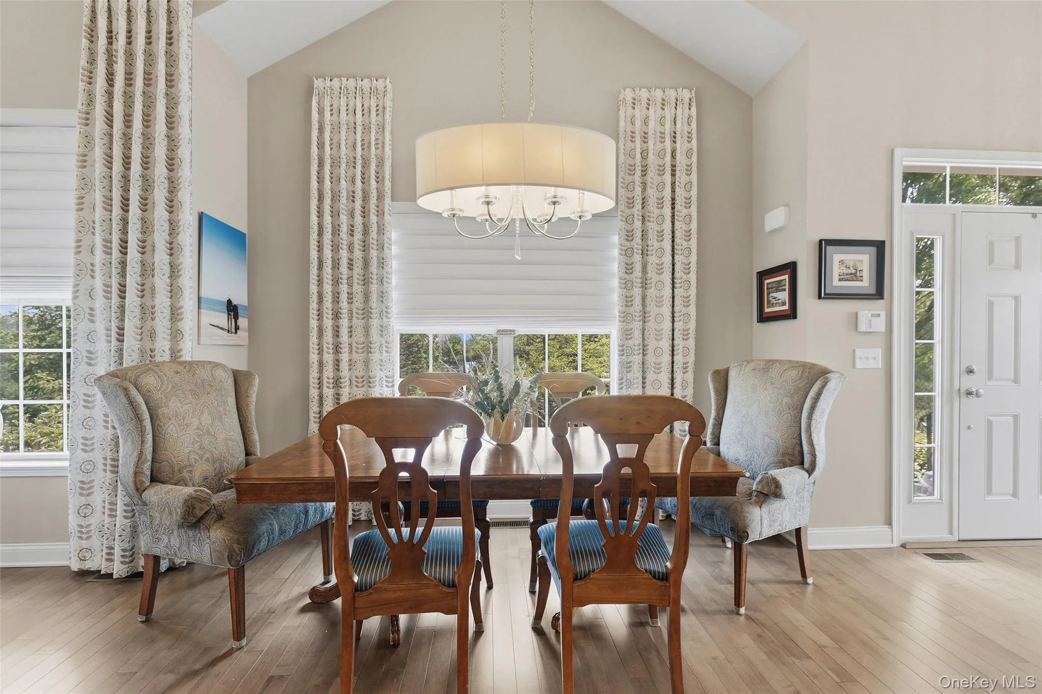 Spacious dining area featuring vaulted ceilings, wood-finish flooring, and multiple windows with custom window treatments Spacious dining area featuring vaulted ceilings, wood-finish flooring, and multiple windows with custom window treatments