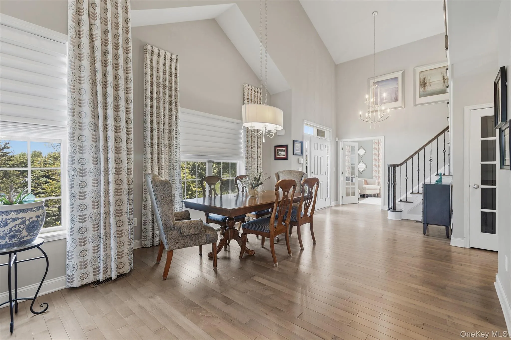 Vaulted ceilings enhance this open-concept room featuring light wood-finish flooring, a tiered chandelier, and a second pendant light Vaulted ceilings enhance this open-concept room featuring light wood-finish flooring, a tiered chandelier, and a second pendant light