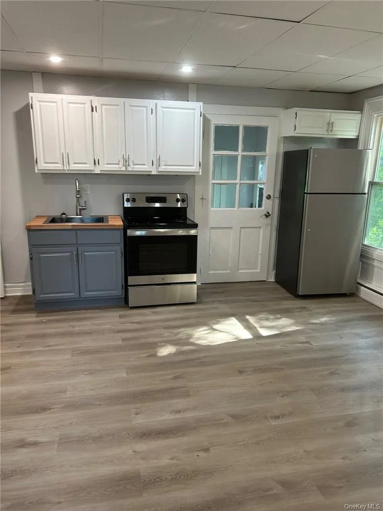 Kitchen with light hardwood / wood-style flooring, stainless steel appliances, a drop ceiling, white cabinetry, and sink Kitchen with light hardwood / wood-style flooring, stainless steel appliances, a drop ceiling, white cabinetry, and sink