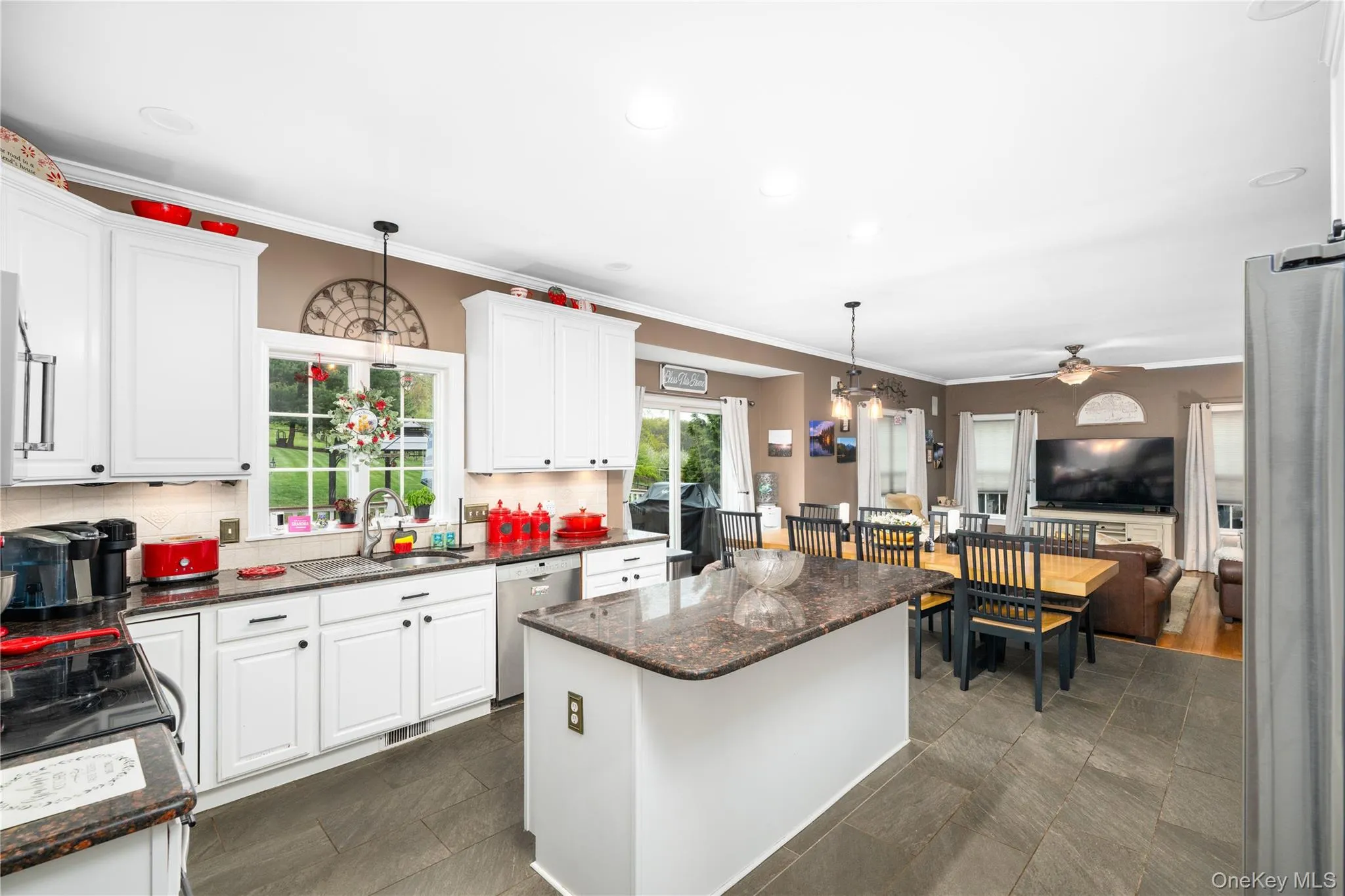 Open-concept kitchen featuring white cabinetry, granite countertops, a central island with integrated storage, and large format tile flooring Open-concept kitchen featuring white cabinetry, granite countertops, a central island with integrated storage, and large format tile flooring