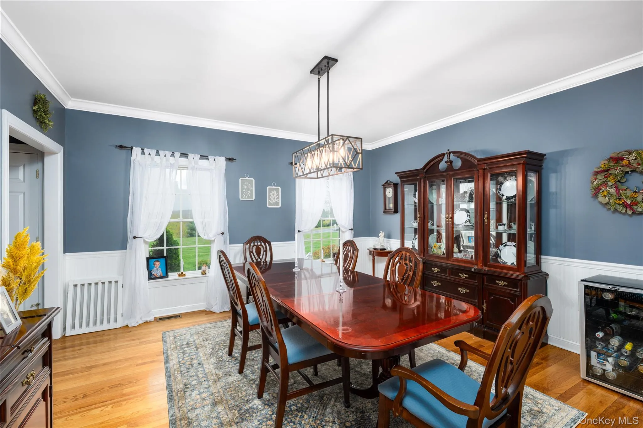 Hardwood flooring complements the wainscoting and crown molding in this room, featuring a geometric chandelier Hardwood flooring complements the wainscoting and crown molding in this room, featuring a geometric chandelier