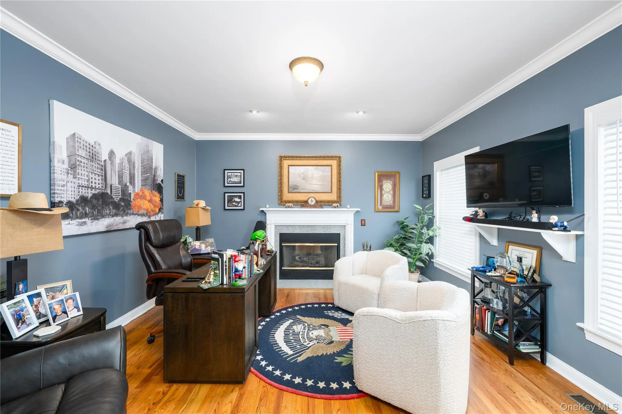 Spacious interior room featuring hardwood flooring, a gas fireplace with a white mantel, and crown molding Spacious interior room featuring hardwood flooring, a gas fireplace with a white mantel, and crown molding