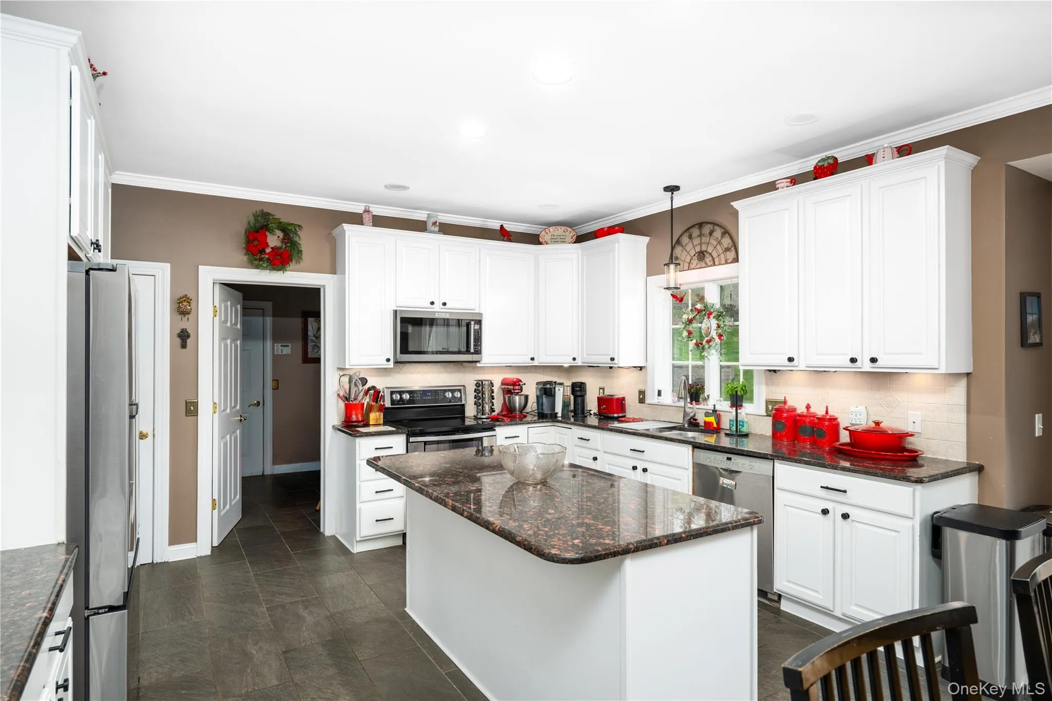 Kitchen featuring white cabinetry, dark granite countertops, stainless steel appliances, a central island, and dark tile flooring Kitchen featuring white cabinetry, dark granite countertops, stainless steel appliances, a central island, and dark tile flooring