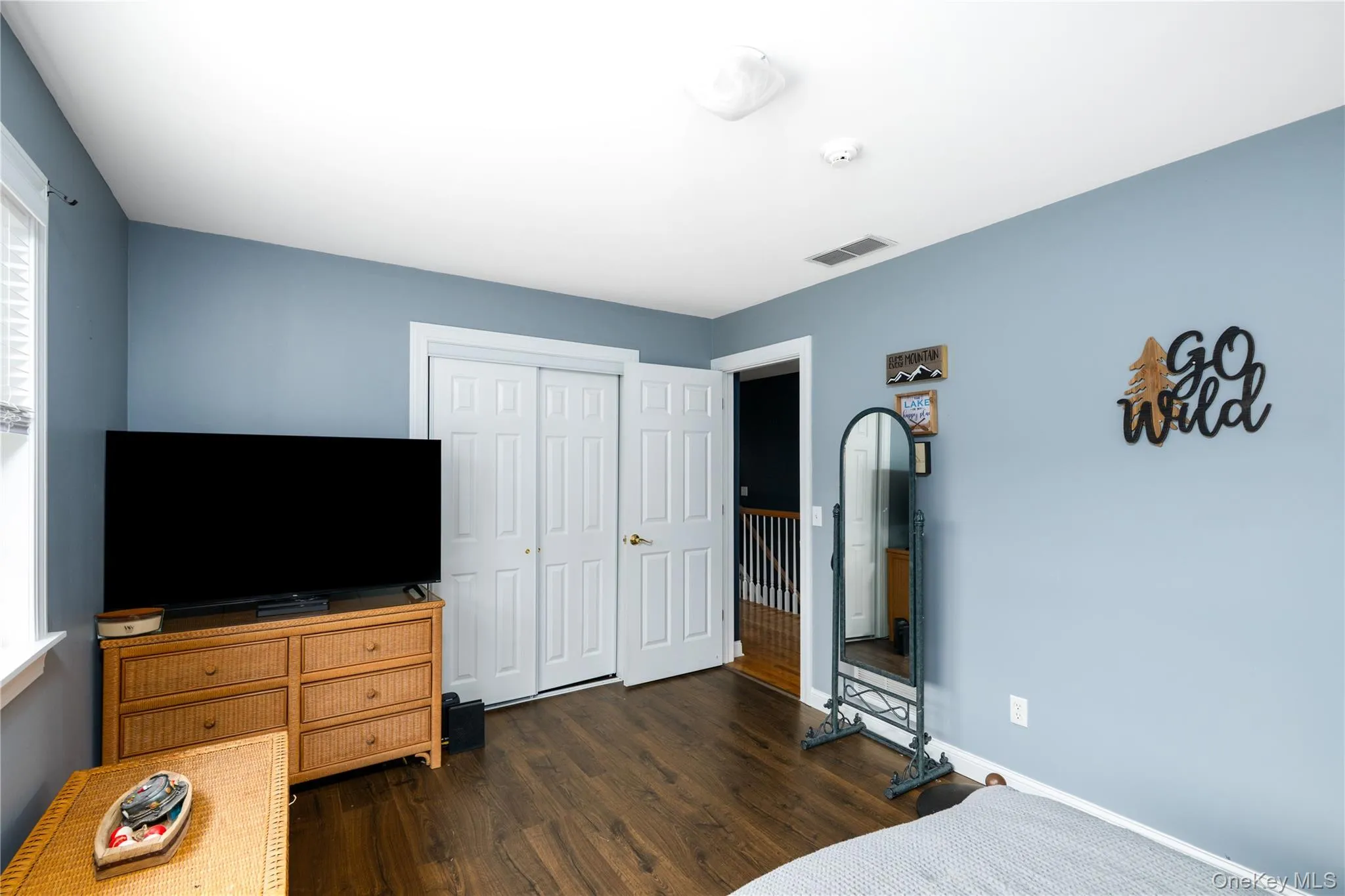 Bedroom featuring wood-finish flooring, light blue walls, a white trim window, and white bi-fold closet doors Bedroom featuring wood-finish flooring, light blue walls, a white trim window, and white bi-fold closet doors