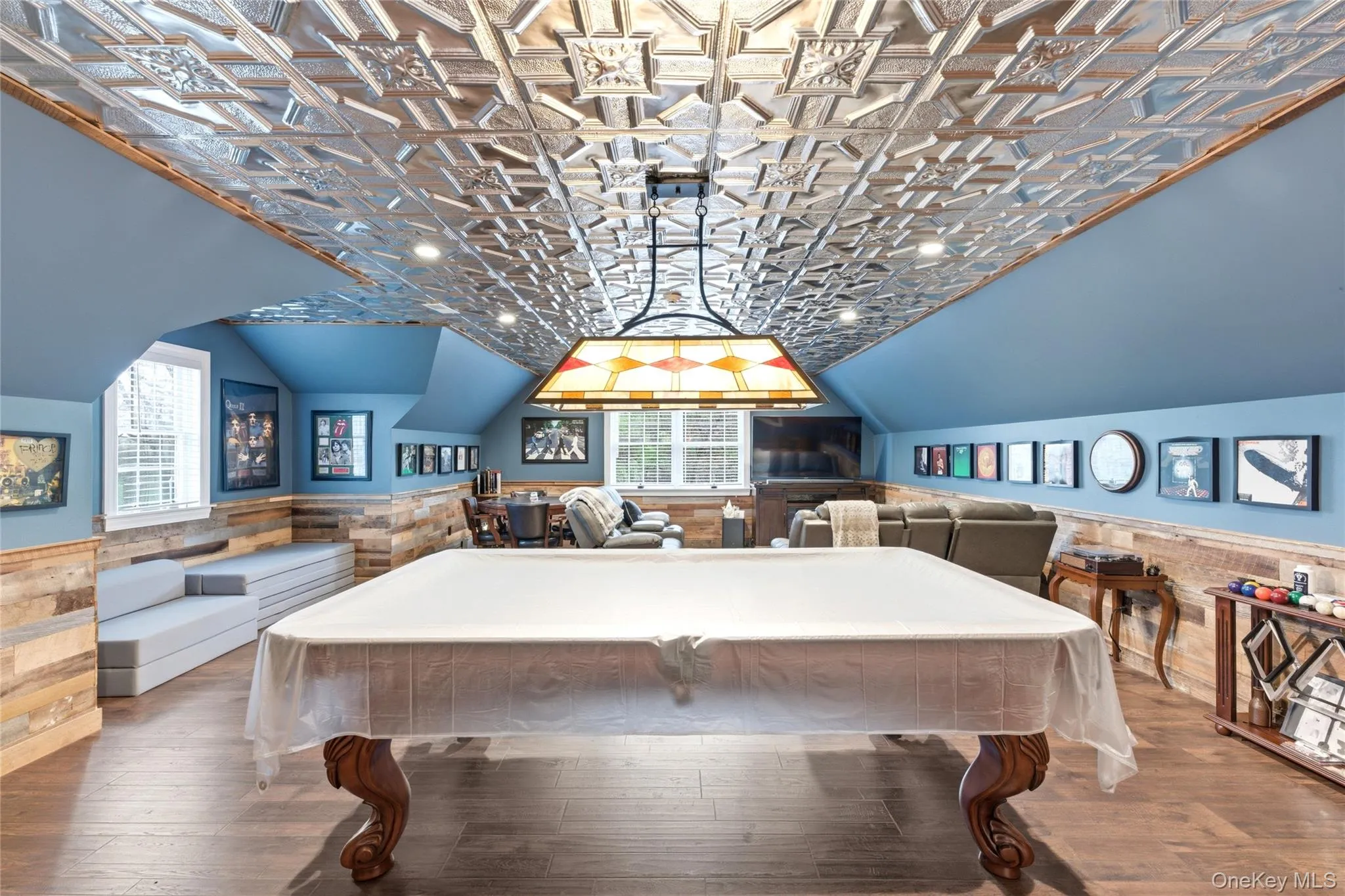 Spacious recreation room featuring wood-finish flooring, a decorative embossed tin ceiling, and a stained glass light fixture Spacious recreation room featuring wood-finish flooring, a decorative embossed tin ceiling, and a stained glass light fixture