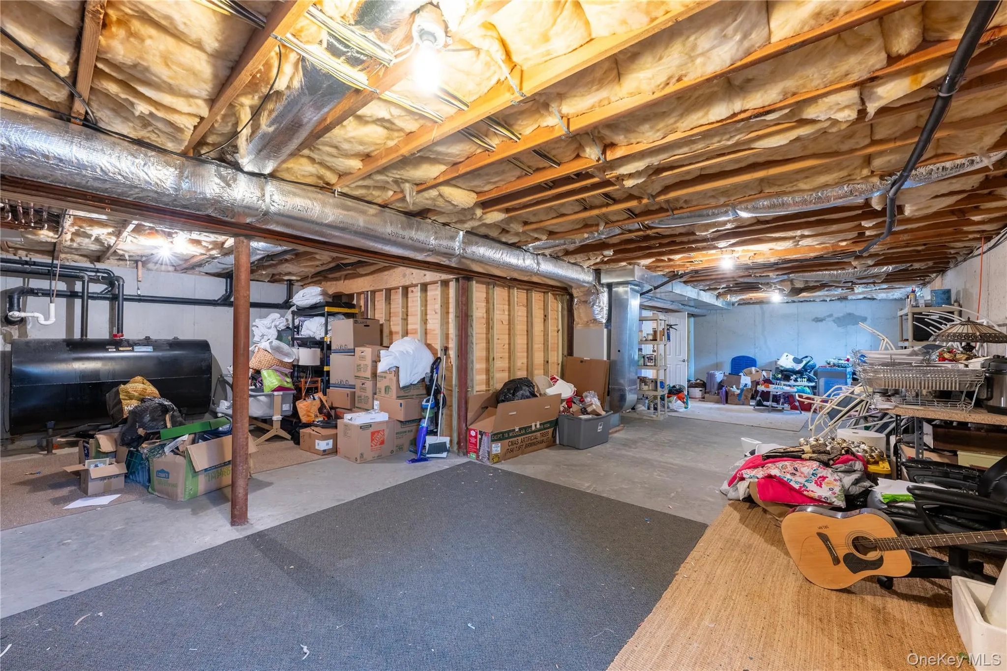 Unfinished lower level with exposed ceiling joists and insulation, concrete flooring, and a visible heating oil tank Unfinished lower level with exposed ceiling joists and insulation, concrete flooring, and a visible heating oil tank