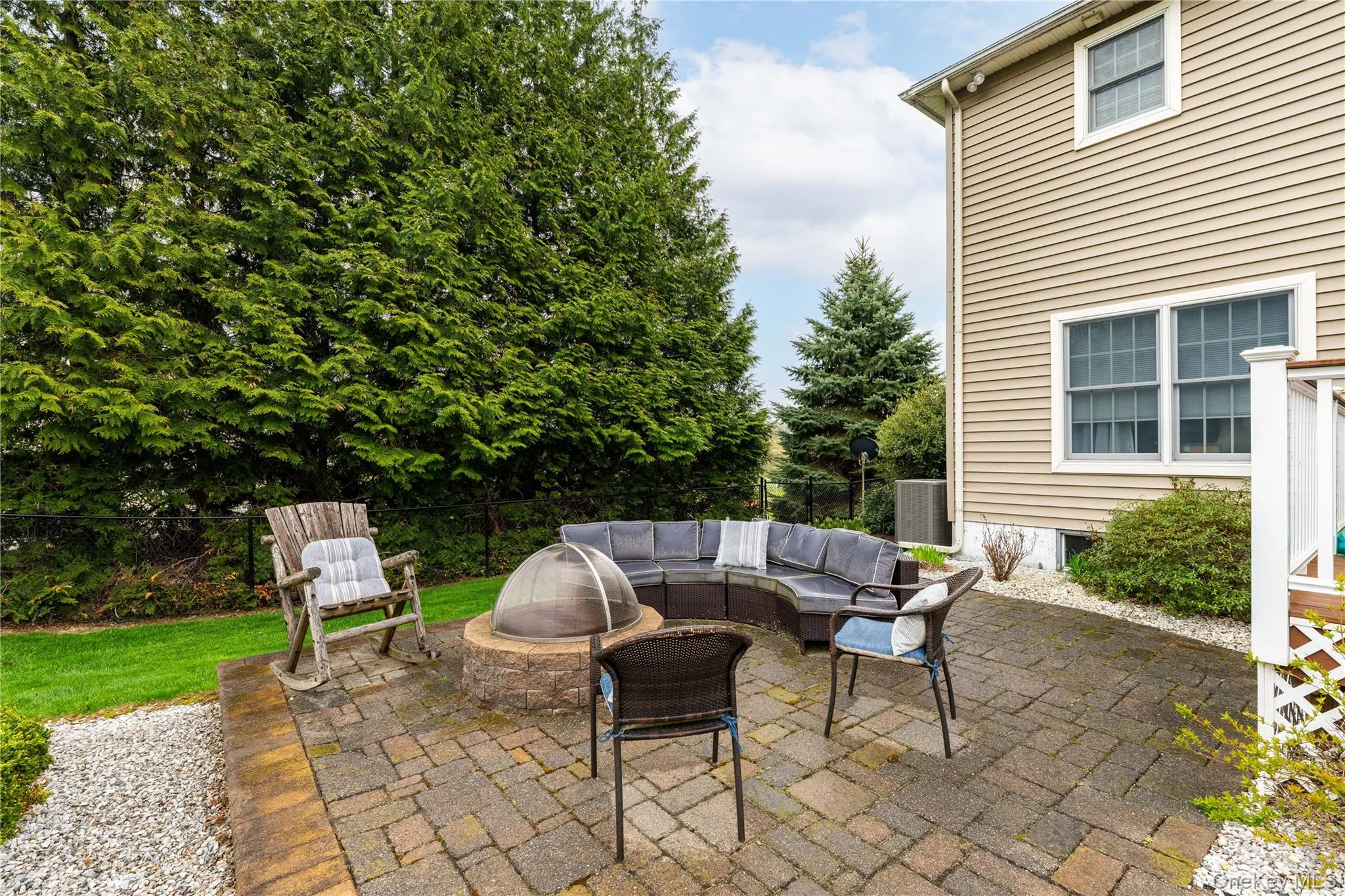 Paver patio with a built-in stone fire pit, bordered by a gravel path and mature evergreen trees Paver patio with a built-in stone fire pit, bordered by a gravel path and mature evergreen trees