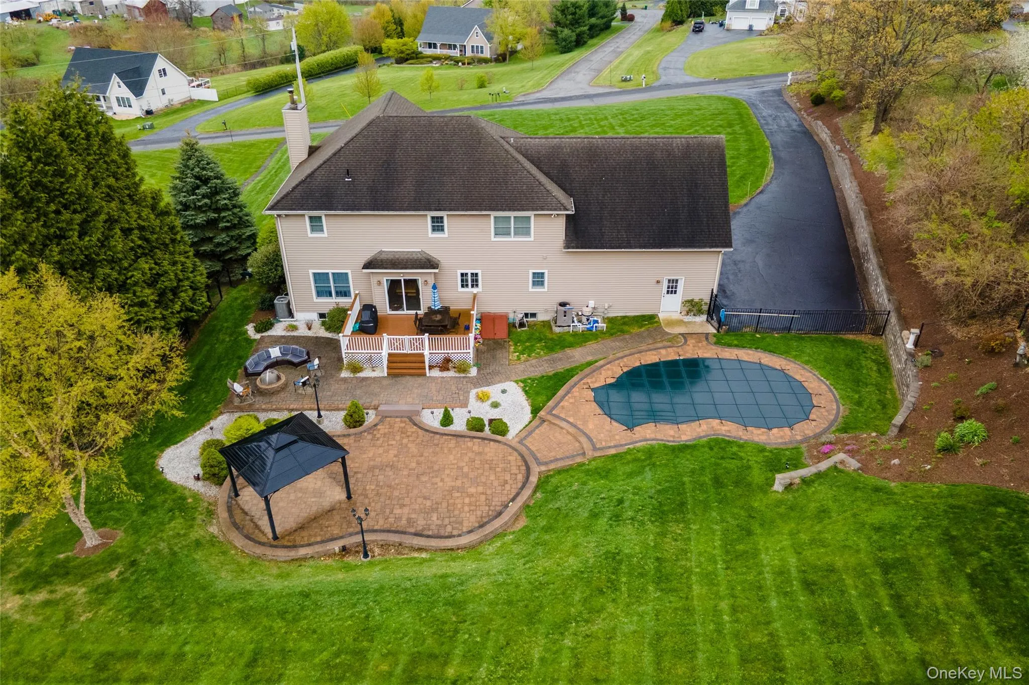 Rear exterior featuring a multi-level composite deck, an expansive paver patio with a gazebo, and a freeform swimming pool with a hard cover Rear exterior featuring a multi-level composite deck, an expansive paver patio with a gazebo, and a freeform swimming pool with a hard cover