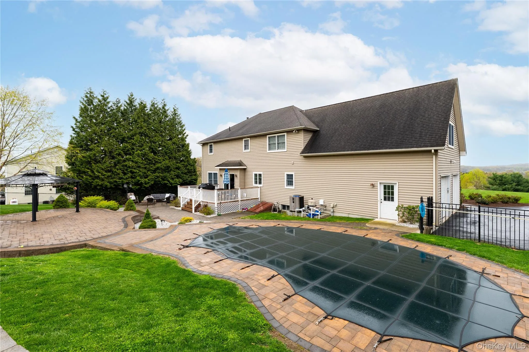 Expansive backyard featuring a covered pool with paver surround, multiple paver patio areas, a raised Trex deck, and a built-in two-car garage Expansive backyard featuring a covered pool with paver surround, multiple paver patio areas, a raised Trex deck, and a built-in two-car garage