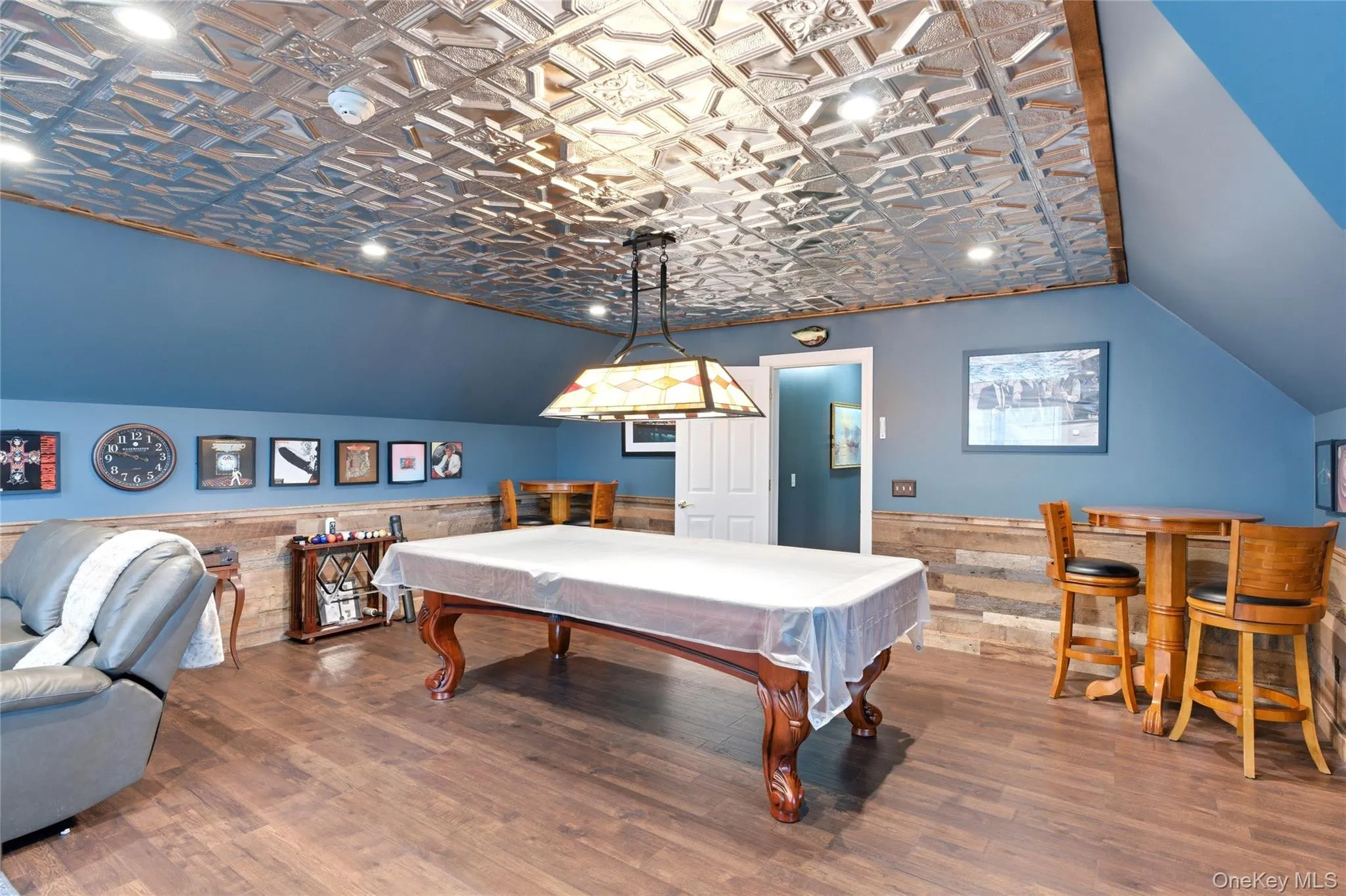 Recreation room featuring a decorative embossed tin-ceiling, rich wood-finish flooring, and shiplap wall accents Recreation room featuring a decorative embossed tin-ceiling, rich wood-finish flooring, and shiplap wall accents