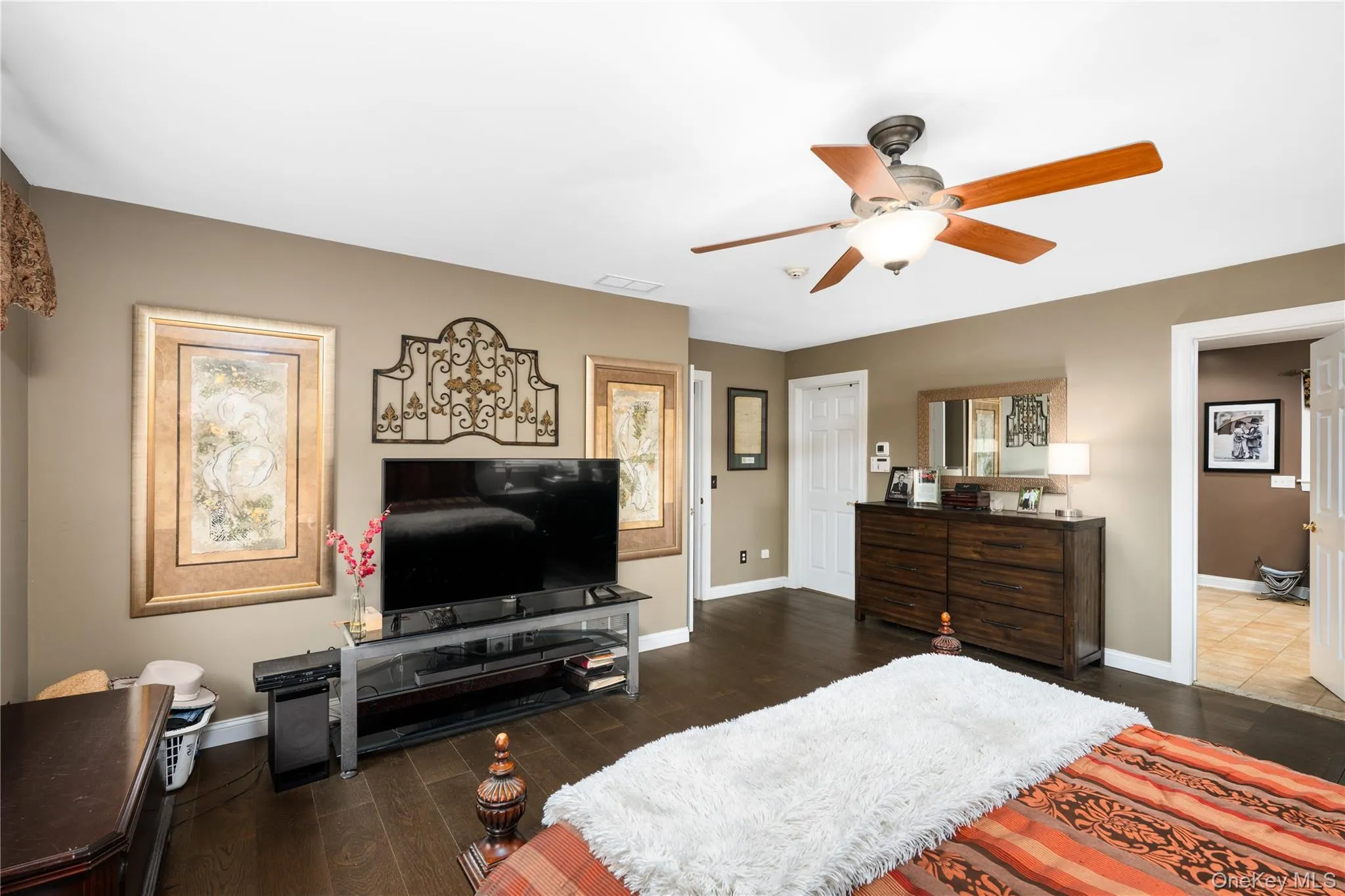 Spacious room featuring dark wood-finish flooring, a ceiling fan with integrated lighting, and a neutral wall color Spacious room featuring dark wood-finish flooring, a ceiling fan with integrated lighting, and a neutral wall color
