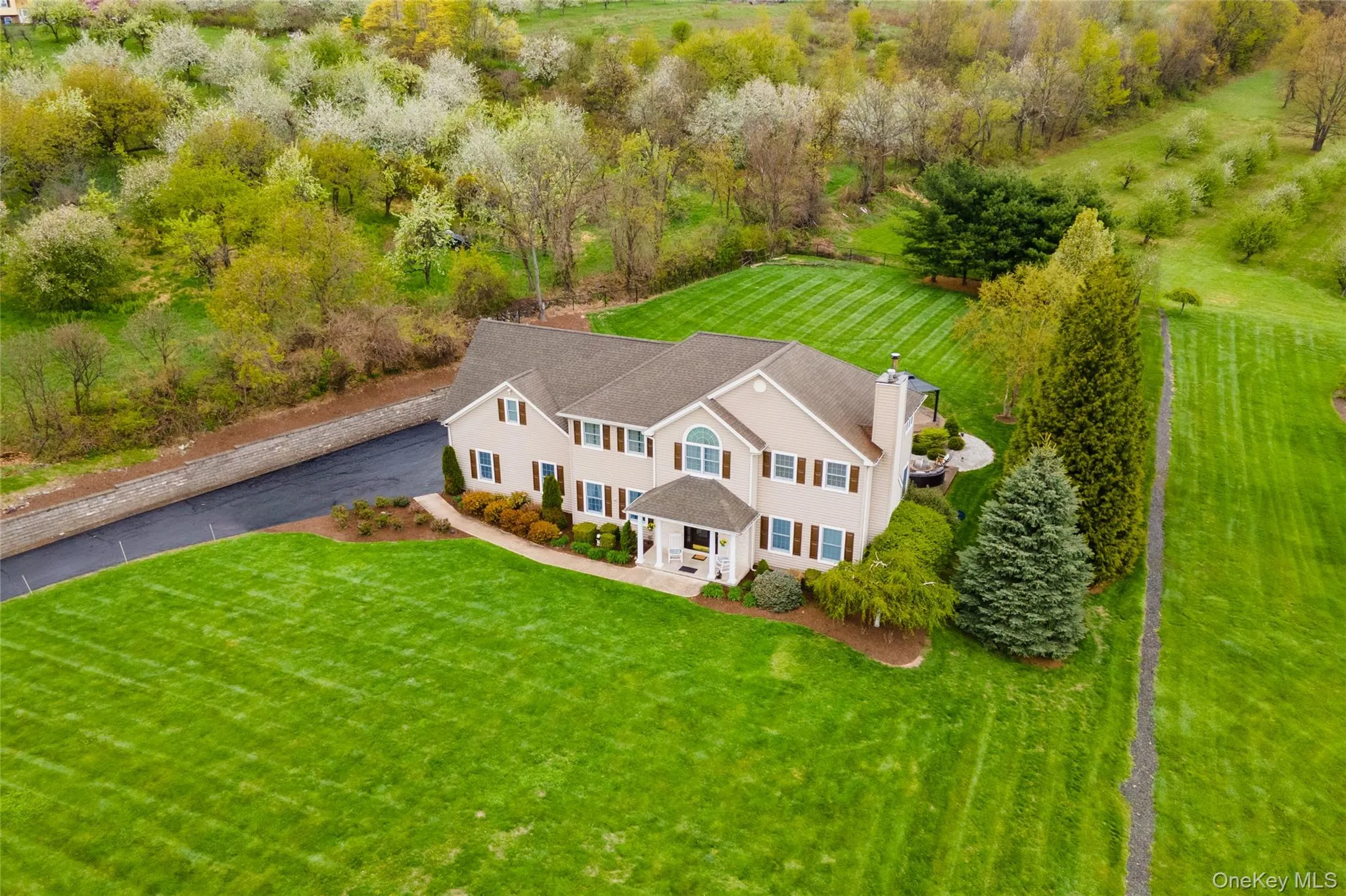 Expansive property featuring a two-story residence with a gabled roof, a large paved driveway, and meticulously manicured lawns Expansive property featuring a two-story residence with a gabled roof, a large paved driveway, and meticulously manicured lawns