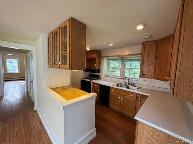 Kitchen featuring wood-finish cabinetry, light-toned countertops, a gas range, a double basin sink, and recessed lighting Kitchen featuring wood-finish cabinetry, light-toned countertops, a gas range, a double basin sink, and recessed lighting