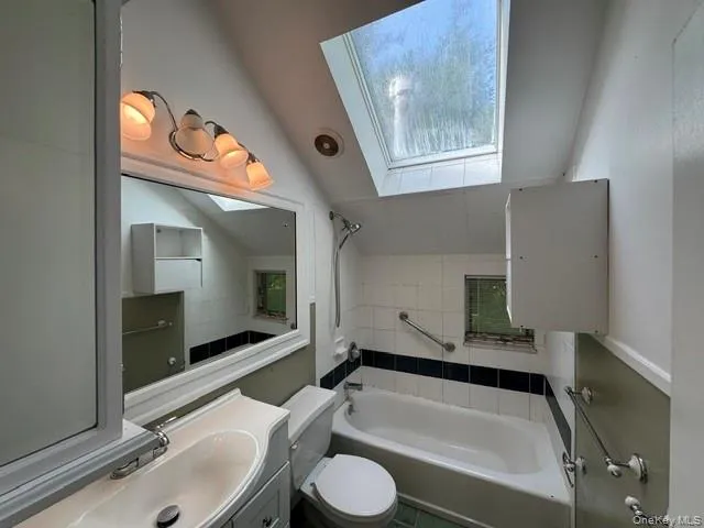 Bathroom featuring a white bathtub, white tiled walls with a black accent stripe, and a skylight Bathroom featuring a white bathtub, white tiled walls with a black accent stripe, and a skylight