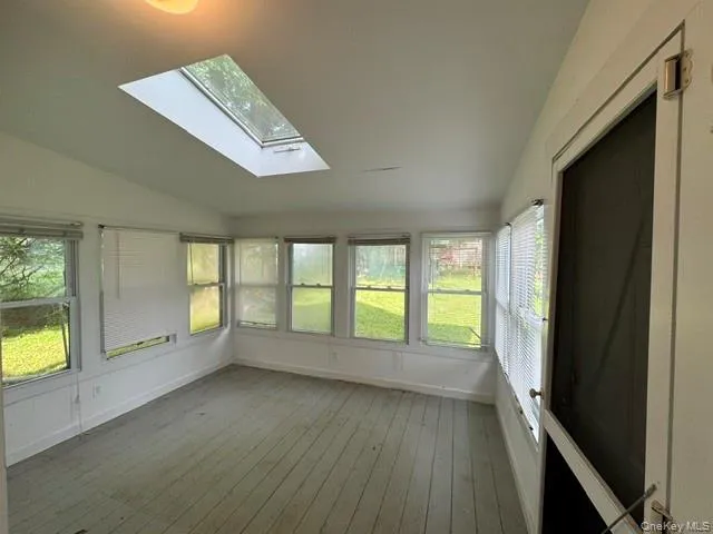 Sunroom featuring a large skylight, multiple windows, painted wood-finish flooring, and a screen door Sunroom featuring a large skylight, multiple windows, painted wood-finish flooring, and a screen door