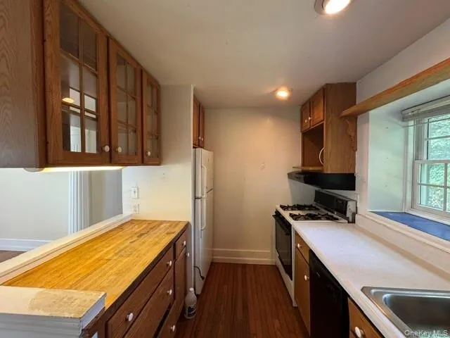 Kitchen featuring wood-finish flooring, oak cabinetry with glass-front uppers, a white refrigerator, a gas range with range hood, and a stainless steel sink Kitchen featuring wood-finish flooring, oak cabinetry with glass-front uppers, a white refrigerator, a gas range with range hood, and a stainless steel sink