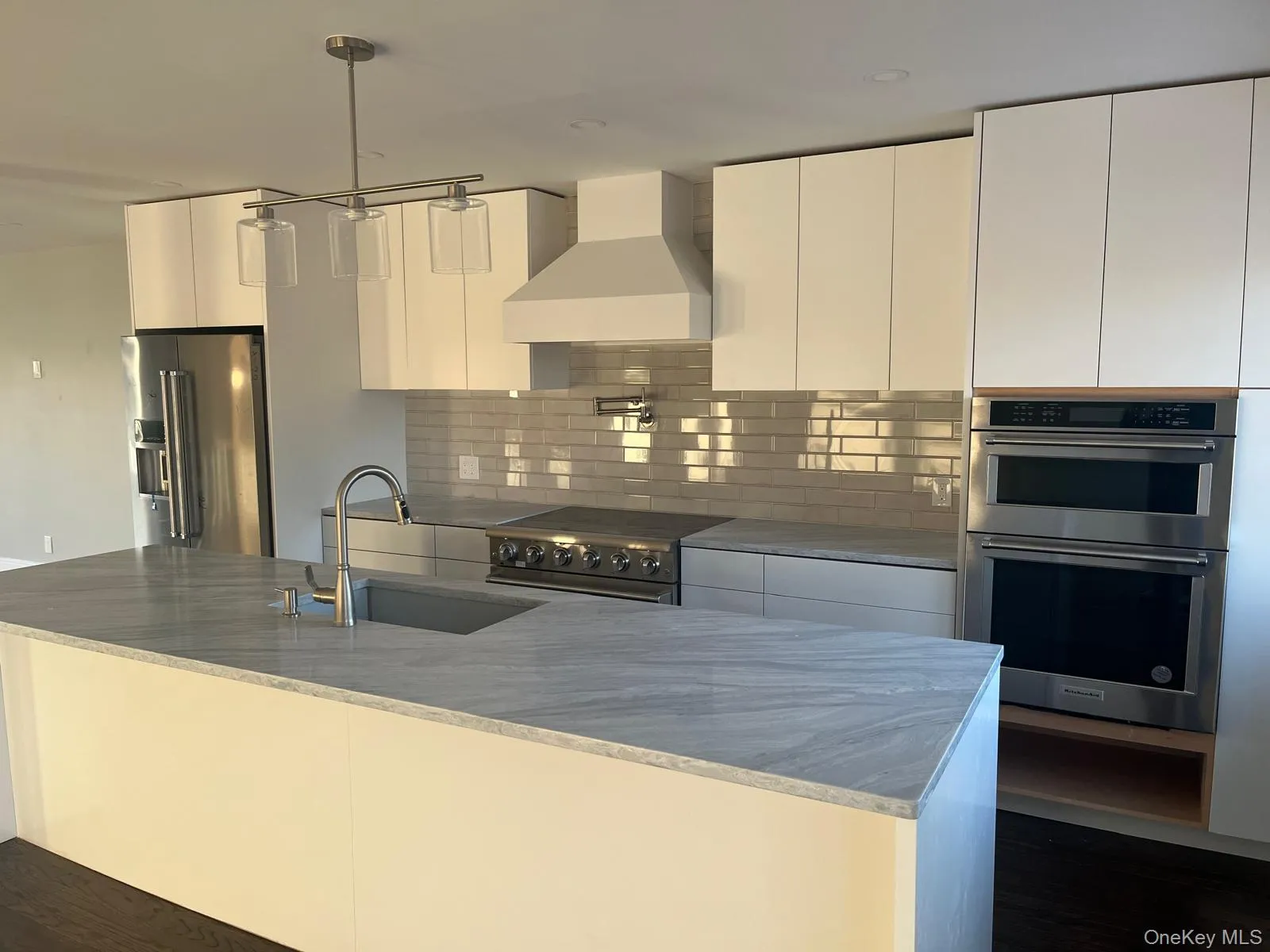 Kitchen with custom exhaust hood, high quality appliances, white cabinets, light stone countertops, and decorative light fixtures Kitchen with custom exhaust hood, high quality appliances, white cabinets, light stone countertops, and decorative light fixtures