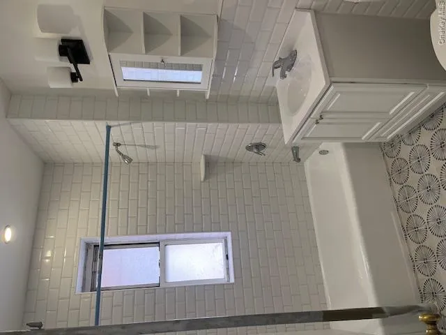 Bathroom featuring white subway tile walls, a white bathtub with a shower, a vanity with under-sink storage, a mirrored medicine cabinet with shelving, and patterned floor tiling Bathroom featuring white subway tile walls, a white bathtub with a shower, a vanity with under-sink storage, a mirrored medicine cabinet with shelving, and patterned floor tiling