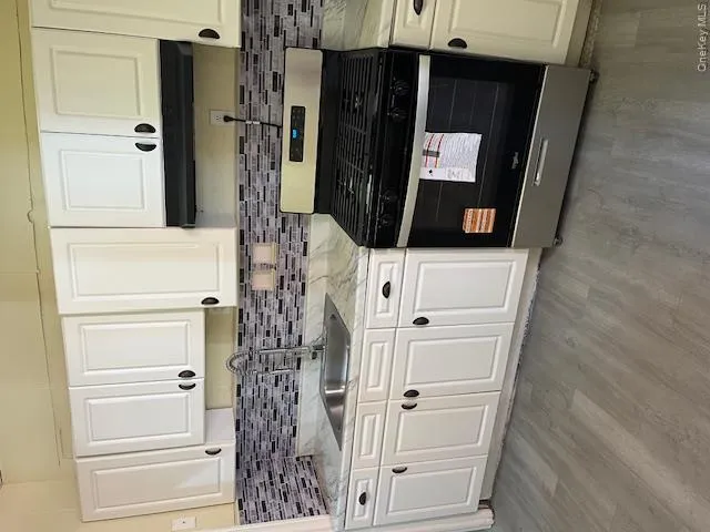 Kitchen featuring white shaker-style cabinetry, a stainless steel gas range, a multi-tone mosaic tile backsplash, light-toned countertops, and wood-finish flooring Kitchen featuring white shaker-style cabinetry, a stainless steel gas range, a multi-tone mosaic tile backsplash, light-toned countertops, and wood-finish flooring