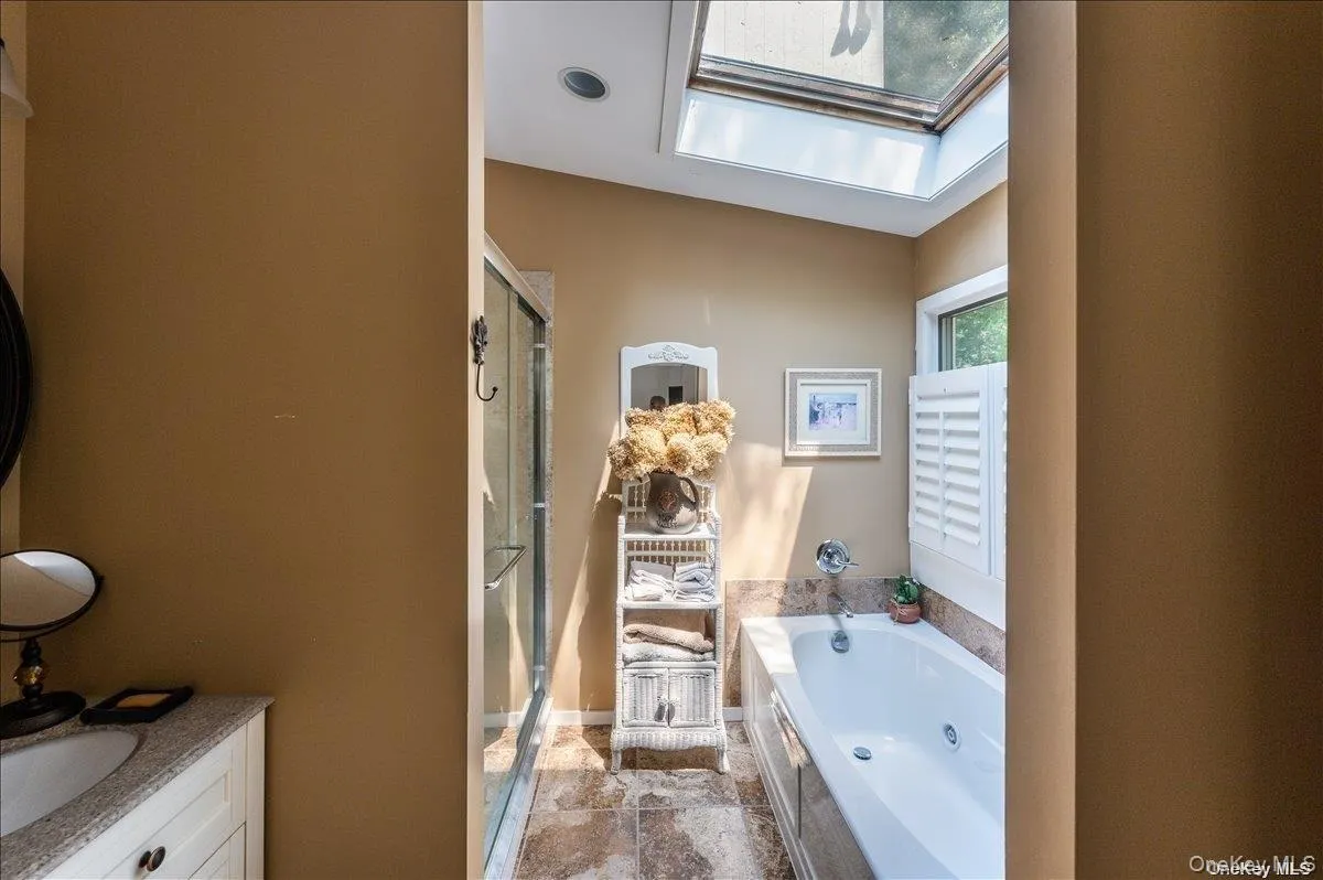 Bathroom featuring a jetted tub, glass-enclosed shower, skylight, and window with plantation shutters Bathroom featuring a jetted tub, glass-enclosed shower, skylight, and window with plantation shutters